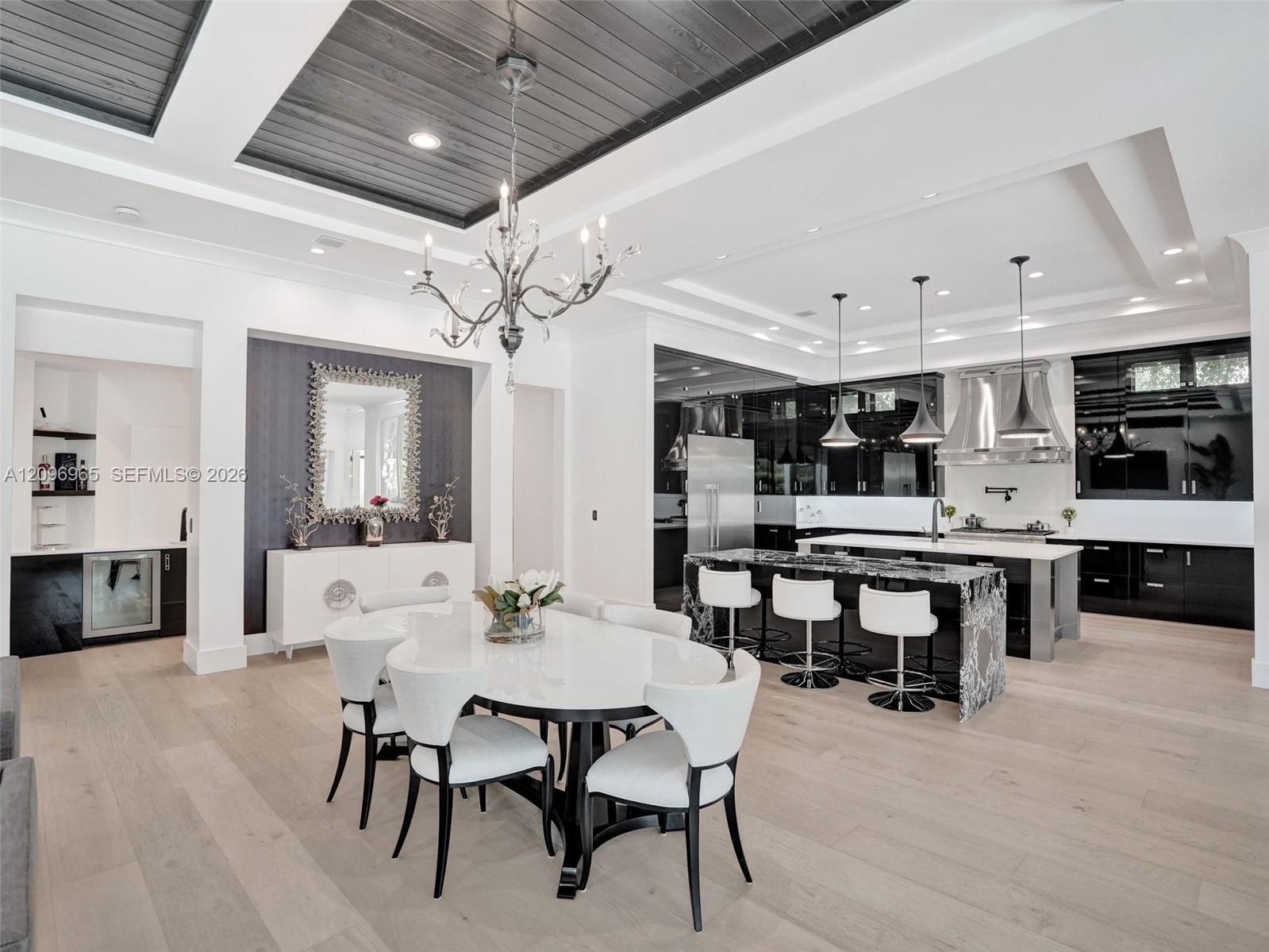Open-concept kitchen and dining area featuring wood-finish flooring, a tray ceiling with charcoal-toned wood plank inlay, a custom kitchen island with