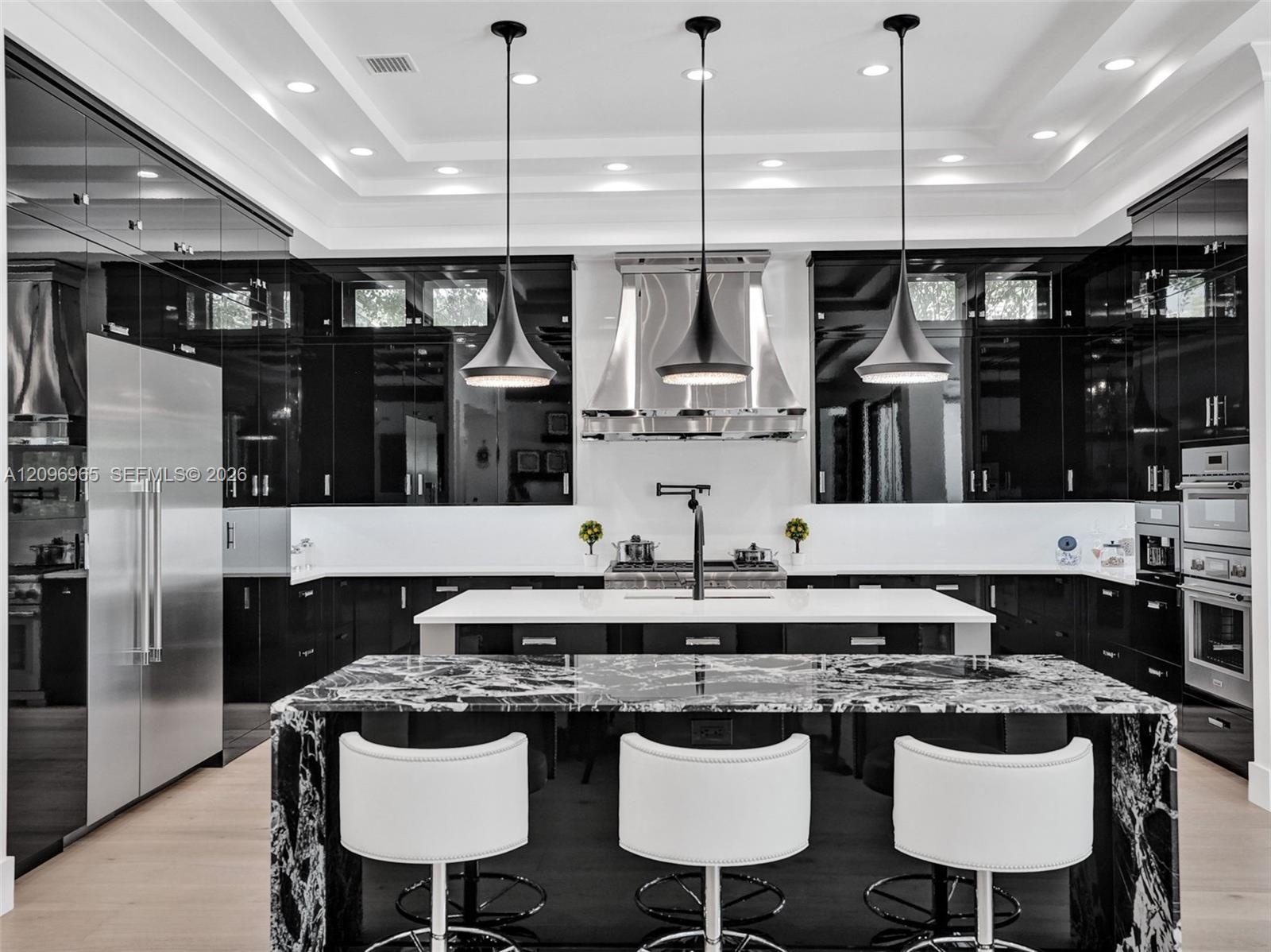 Gourmet kitchen featuring high-gloss black cabinetry, a coffered ceiling, a stone-topped central island, a stainless steel range hood, and a statement