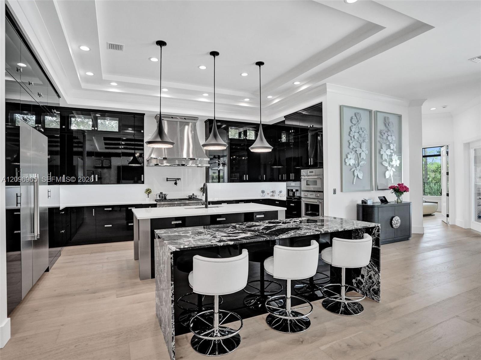 Tray ceiling with dark wood-finish paneling, intricate wrought iron chandelier, recessed lighting, and kitchen island with stone-finish waterfall edge