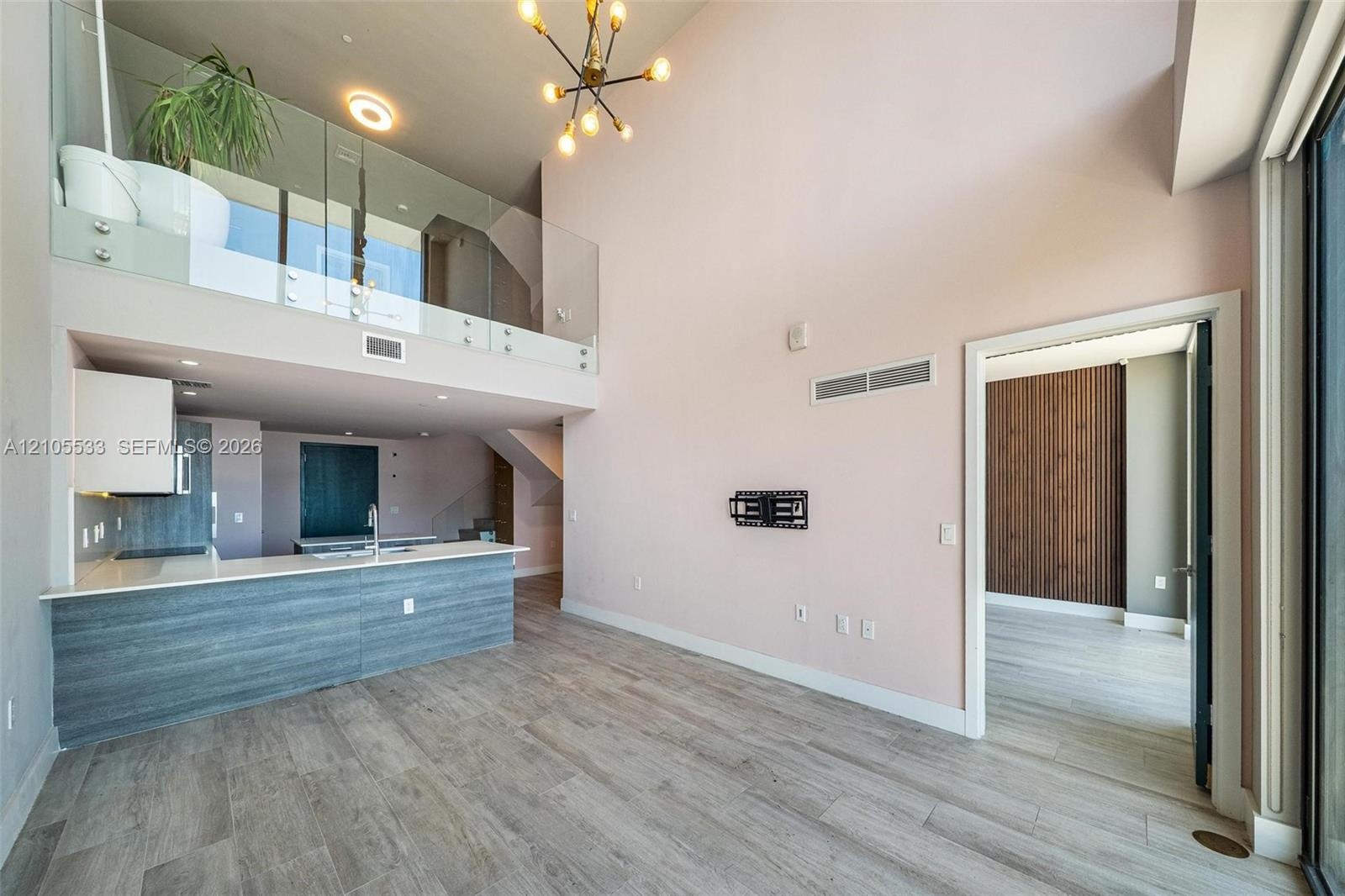 Double-height ceiling, glass-paneled mezzanine railing, wood-finish flooring, kitchen island with solid surface countertop, and modern multi-arm penda