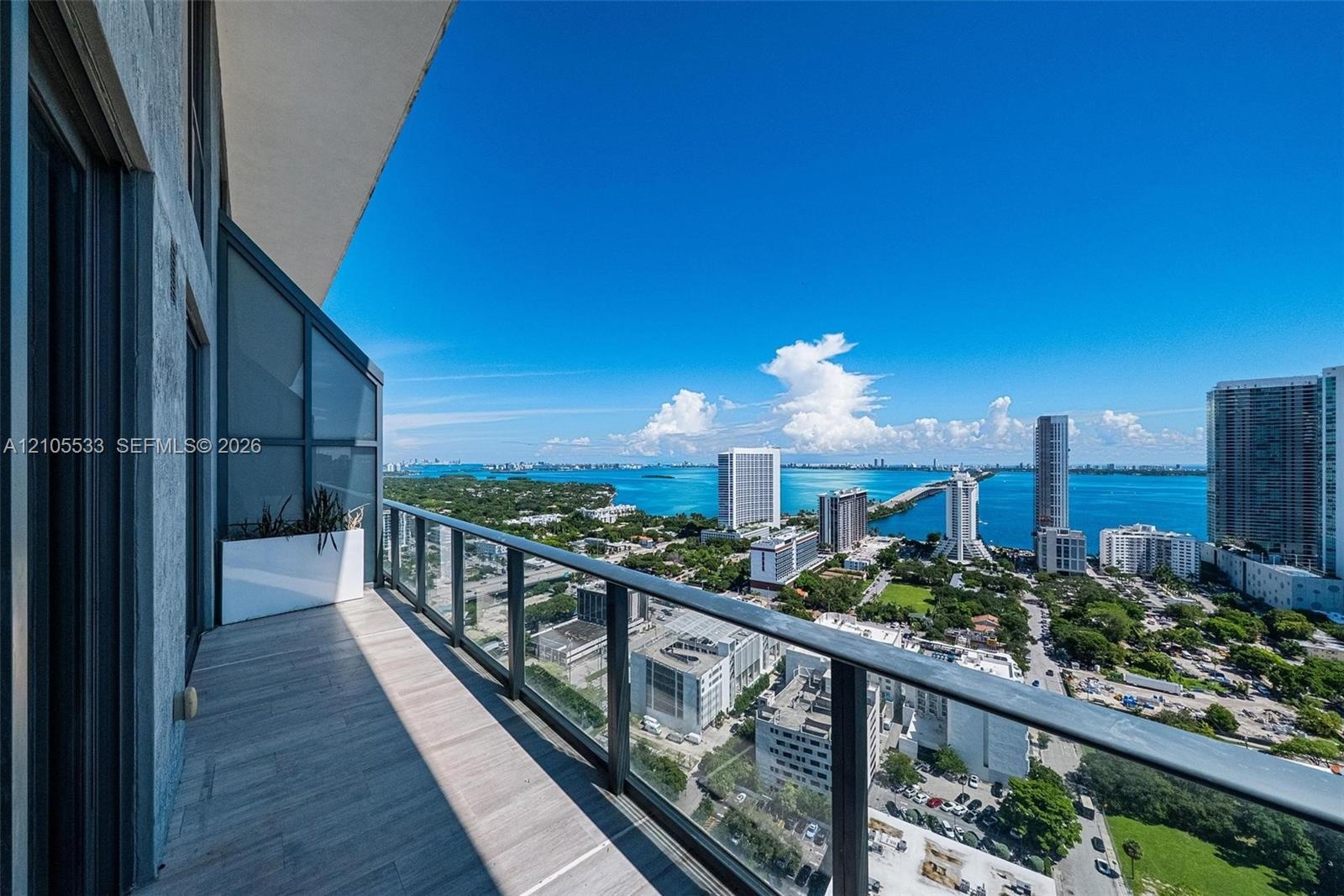 Private balcony featuring wood-finish tile flooring, glass panel railings, and a metal frame