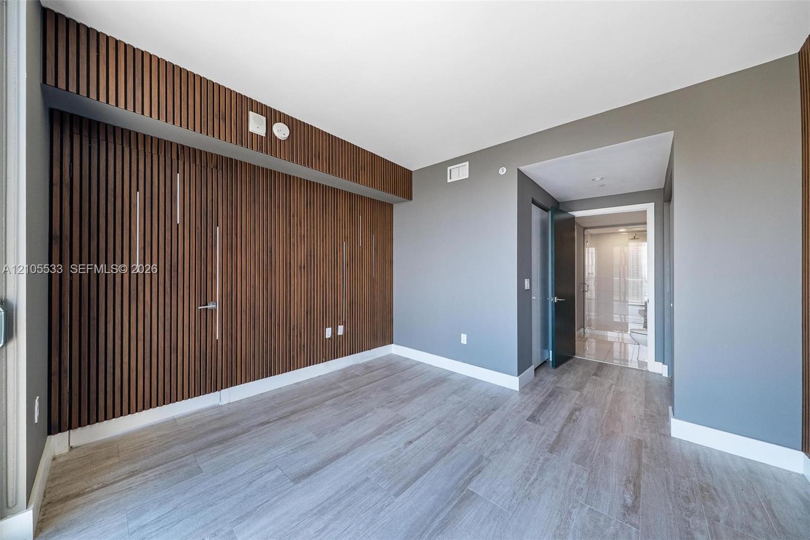 Room featuring a floor-to-ceiling vertical wood-slat accent wall, wood-finish flooring, and solid-core doors