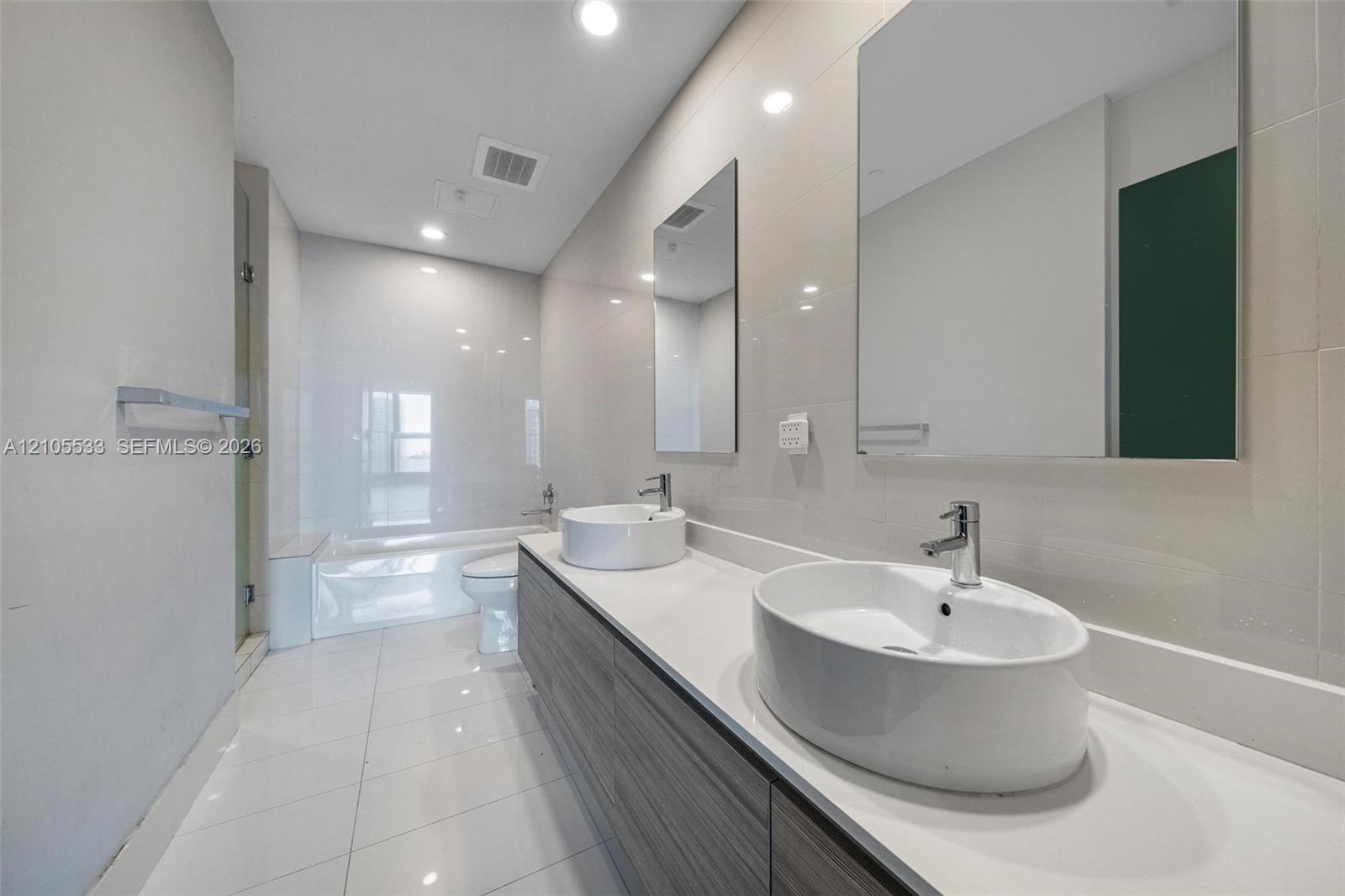 Double vanity featuring wood-finish cabinetry, white countertop, vessel sinks, chrome fixtures, and wall-mounted rectangular mirrors