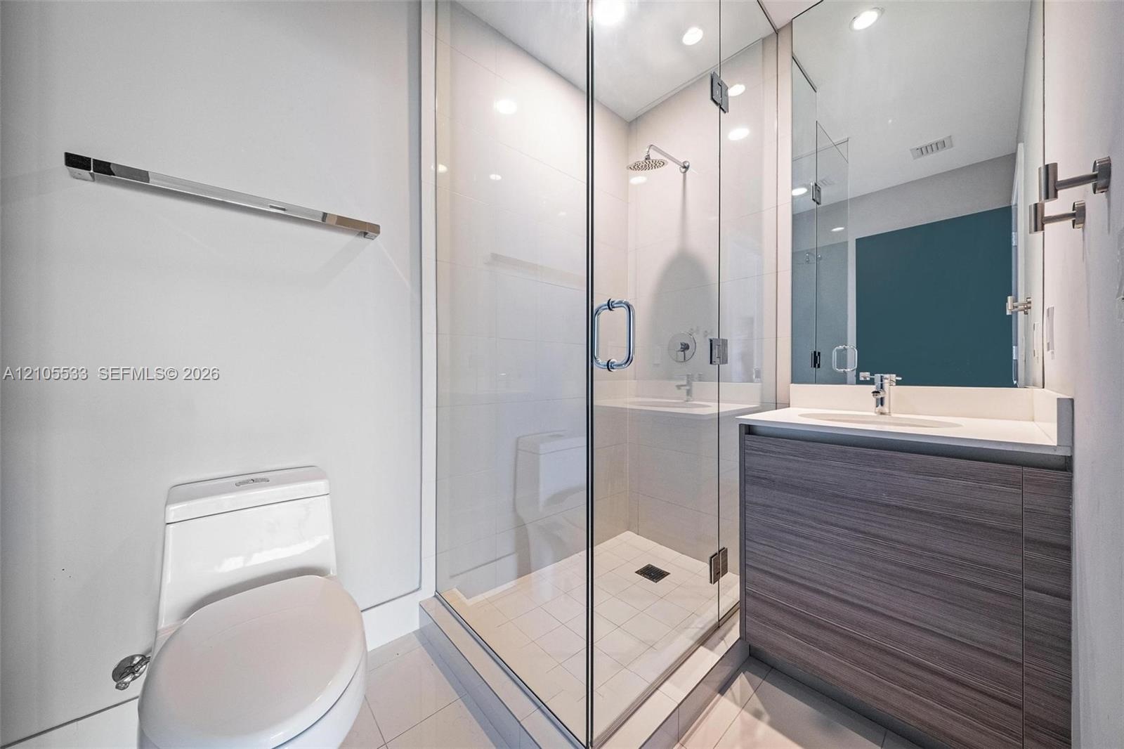 Bathroom featuring a glass-enclosed shower with a rainfall showerhead, a wood-finish vanity with a solid-surface countertop, an integrated sink, and c