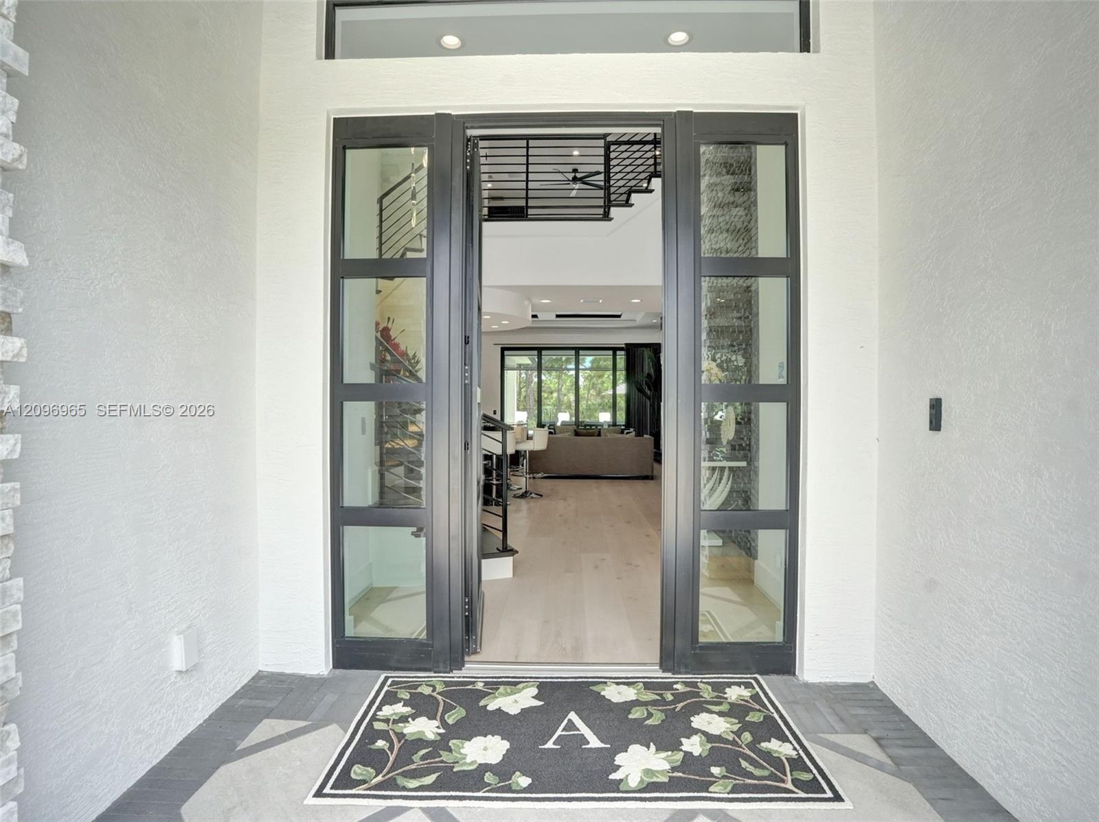 Modern pivot-style entry door featuring a matte black frame with floor-to-ceiling glass paneling and light-toned wood-finish flooring