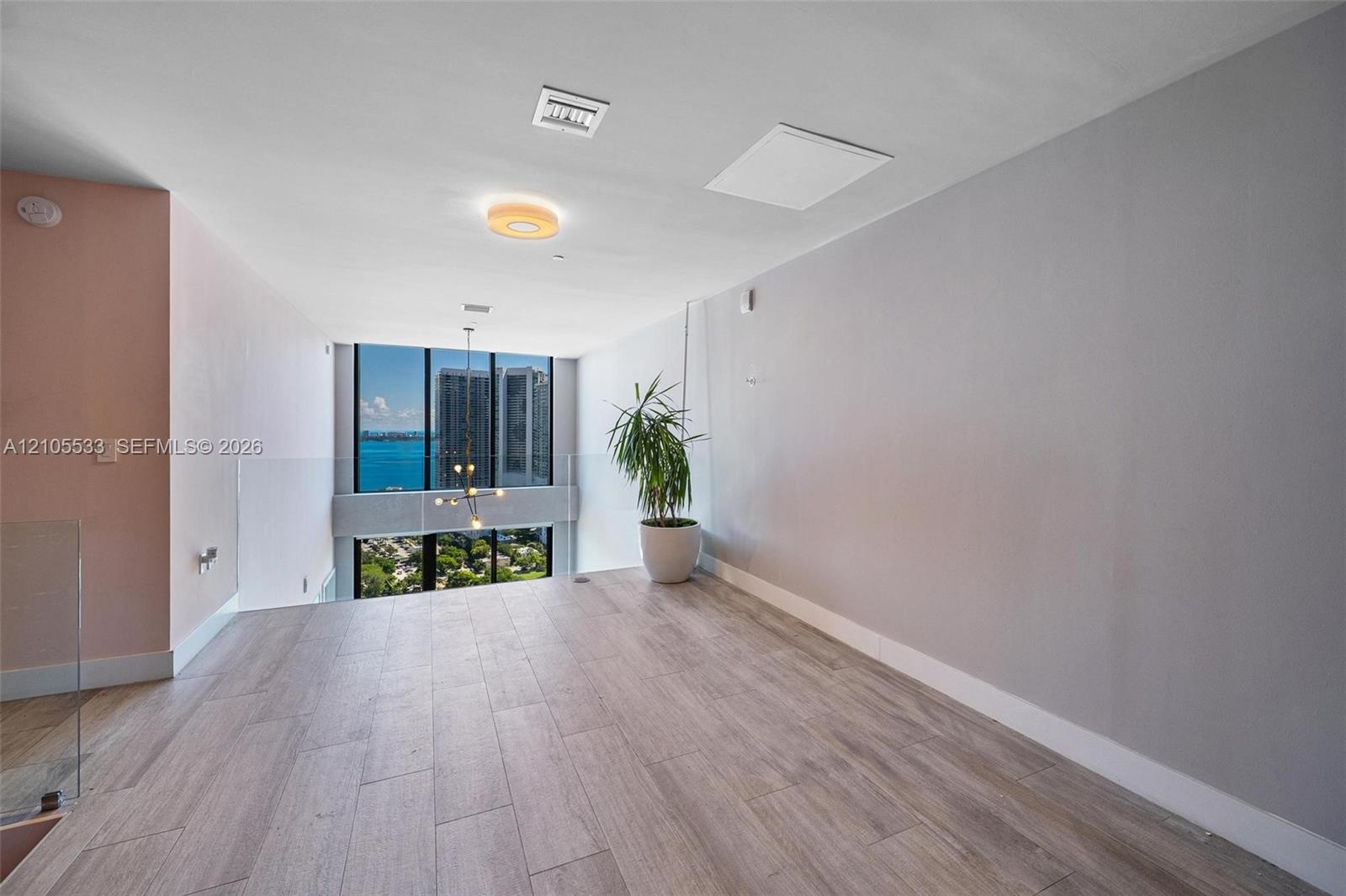 Open-plan interior featuring wood-finish flooring, floor-to-ceiling windows, and a glass panel railing