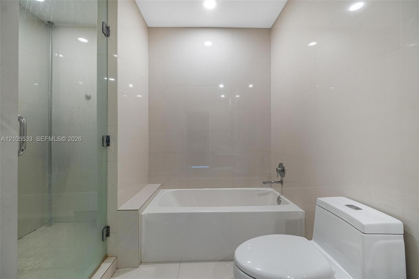 Bathroom featuring a separate glass-enclosed shower, built-in soaking tub with a deck, and large-format tile wall cladding