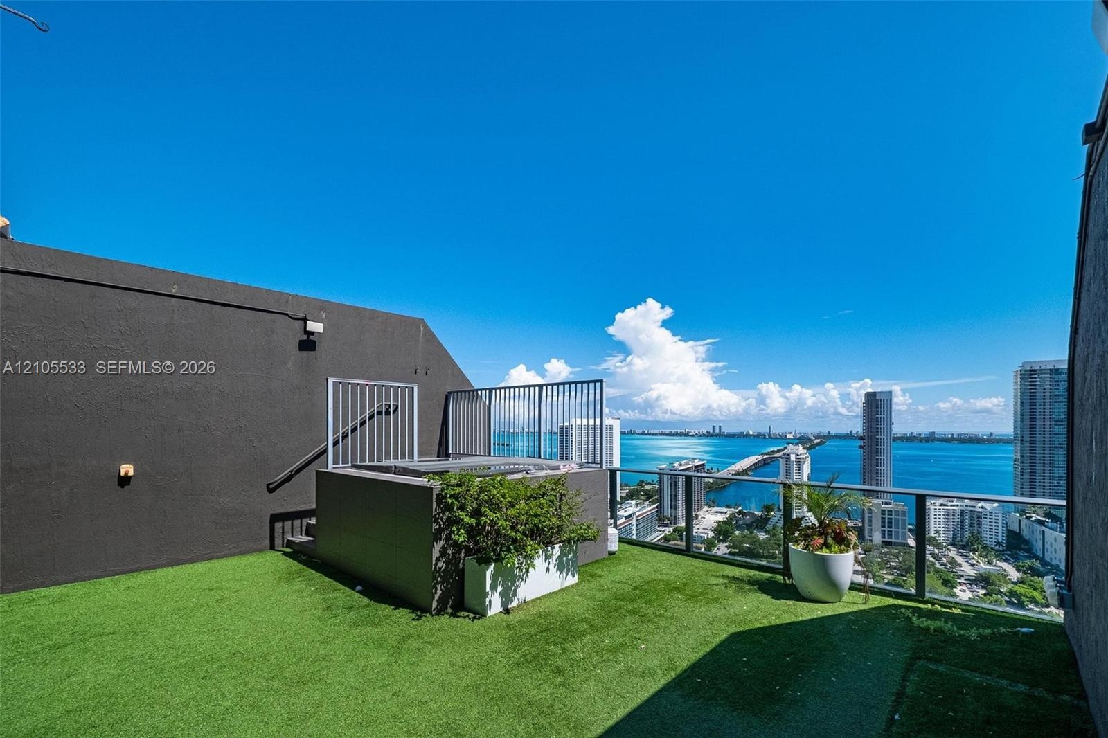 Rooftop terrace featuring synthetic turf, a built-in spa, glass railing, and expansive water and skyline scenery