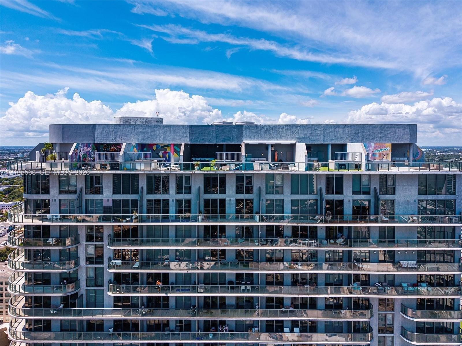 High-rise residential exterior featuring expansive floor-to-ceiling windows, wrap-around glass balconies, and a rooftop terrace level