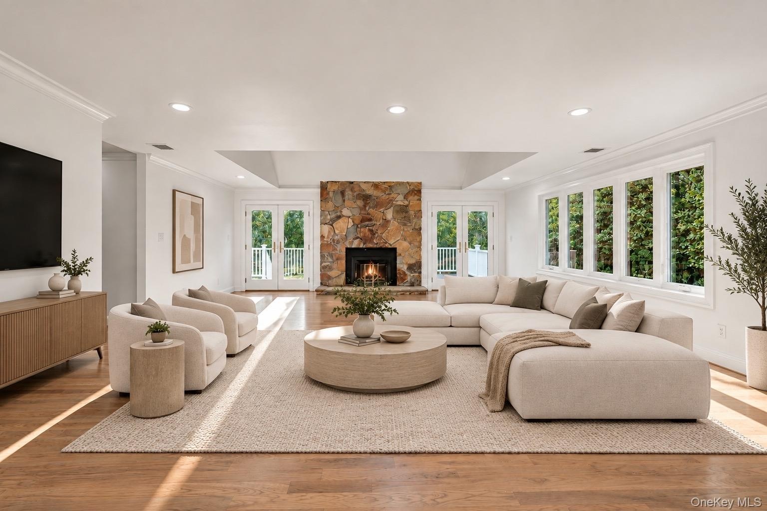Living area featuring wood-finish flooring, a tray ceiling, recessed lighting, expansive multi-pane windows, and a floor-to-ceiling stone fireplace