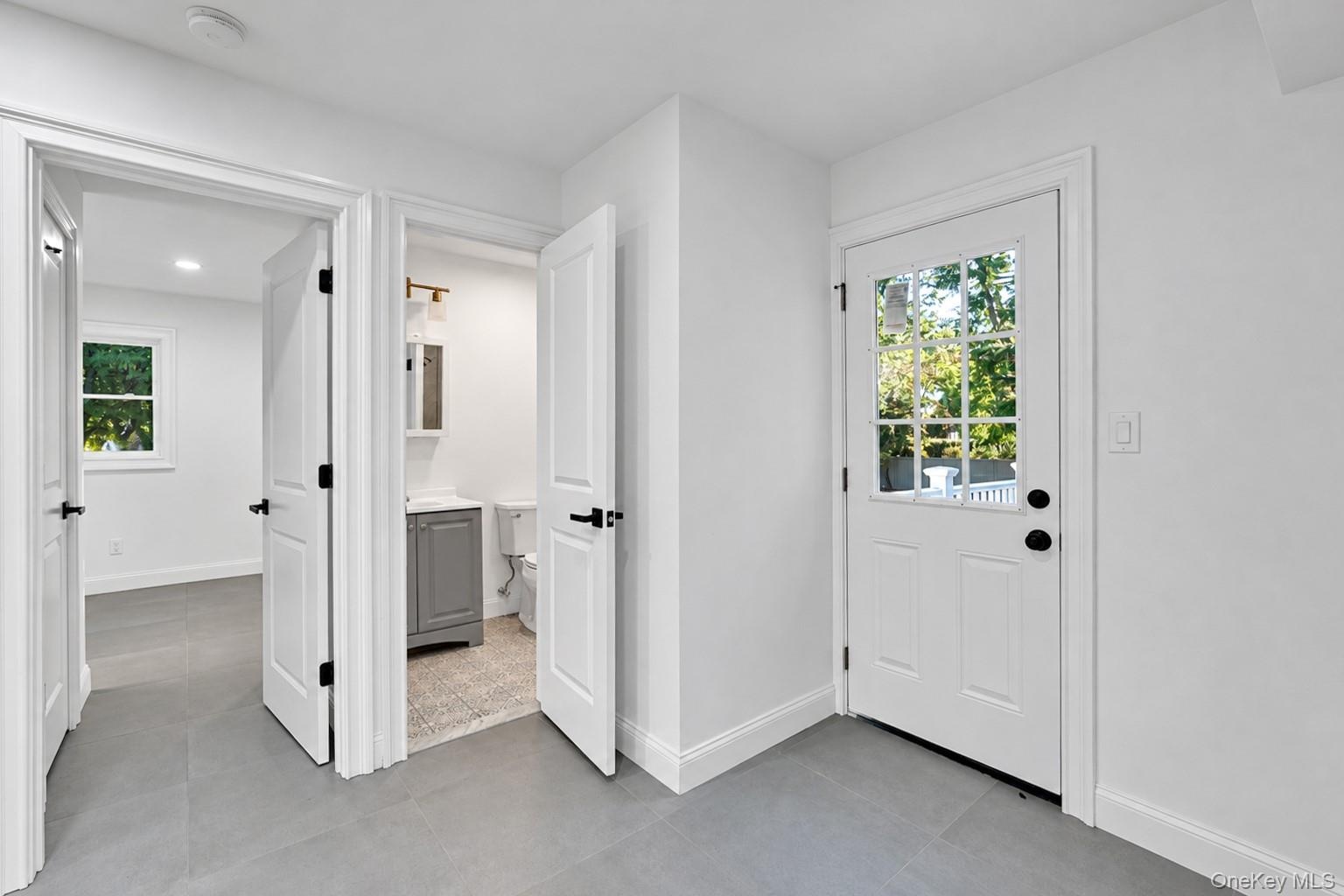 Neutral-toned ceramic tile flooring, solid-core shaker style interior doors with matte black hardware, and an exterior door with a nine-pane window in