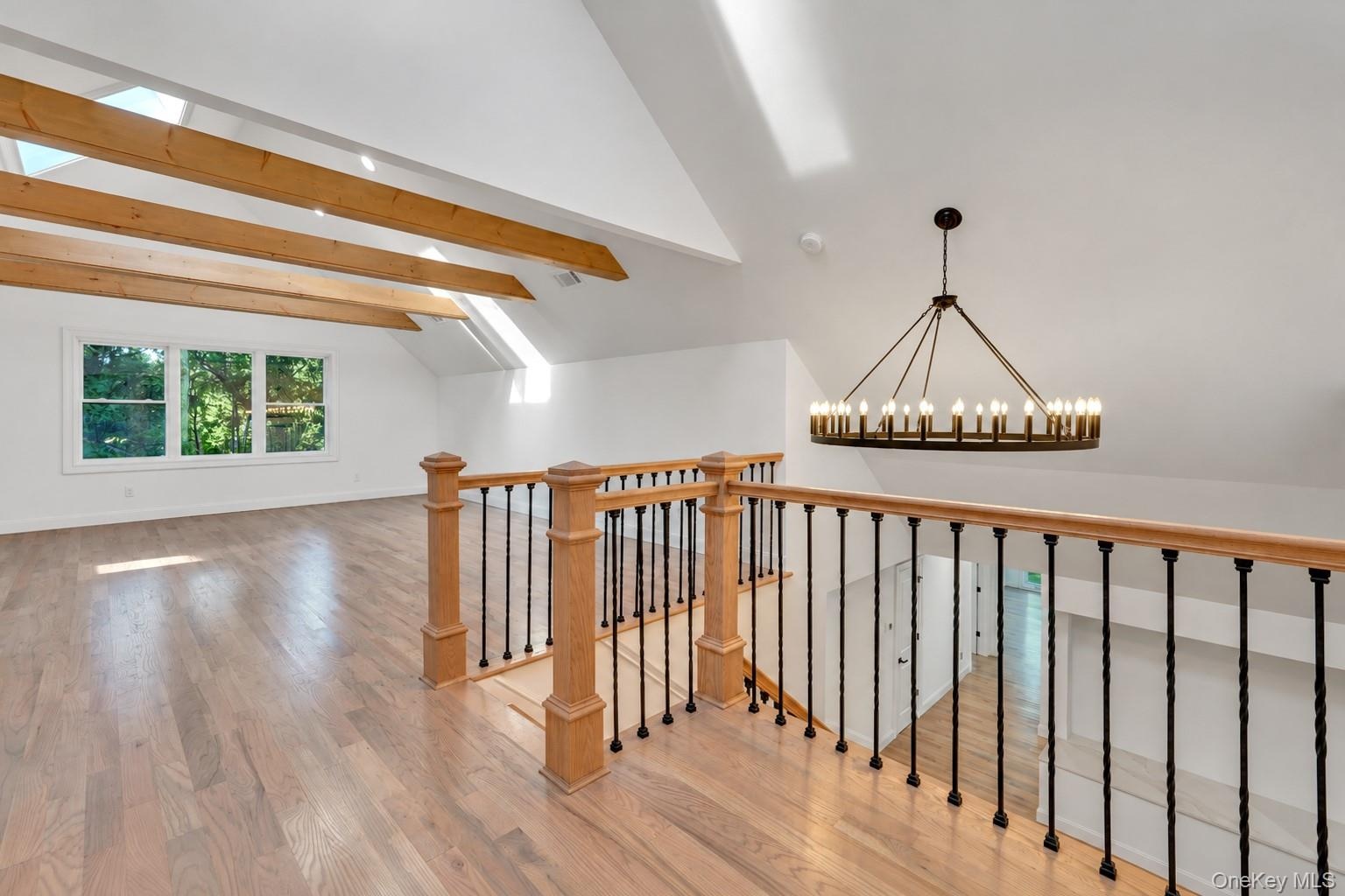Vaulted ceilings featuring exposed timber beams, wood-finish flooring, a large circular wrought iron chandelier, and a custom stair railing with wood 