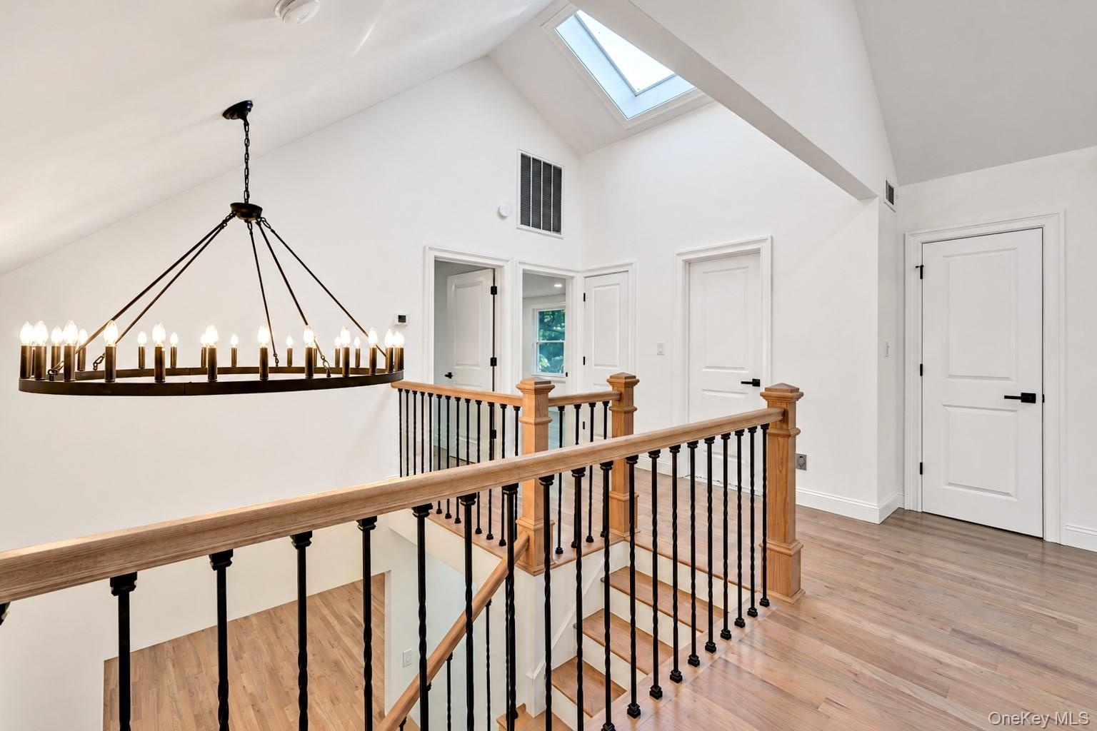 Vaulted ceiling with skylight, wood-finish flooring, and chandelier featuring a circular metal frame with tiered candelabra bulbs