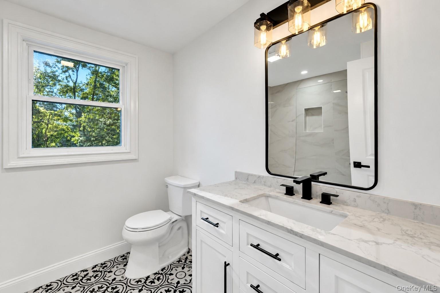 2nd floor Bathroom featuring a white vanity with a stone countertop, an integrated rectangular sink, matte black hardware, and patterned tile flooring