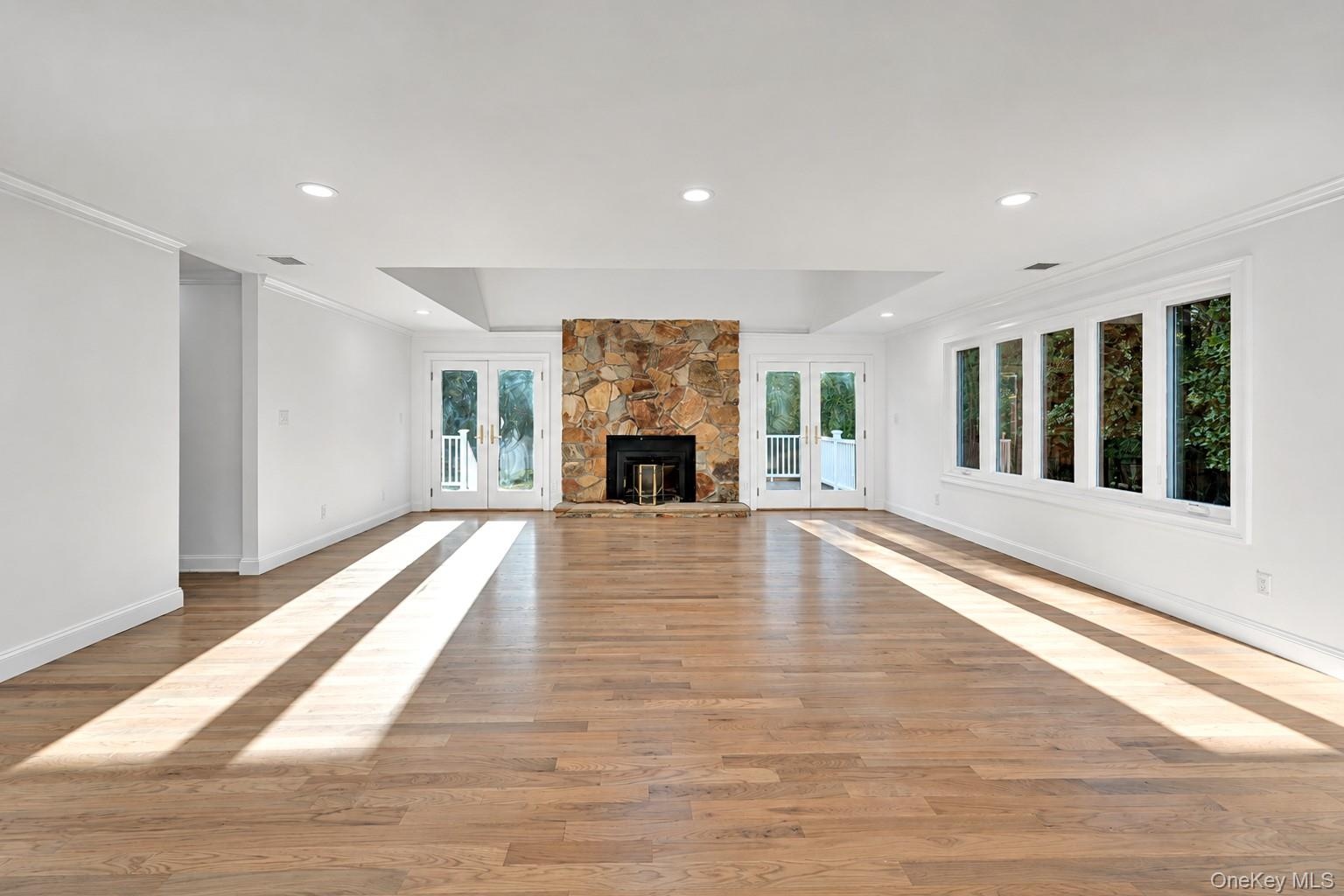 Wood-finish flooring, stone-veneer fireplace with hearth, recessed lighting, multi-pane casement windows, and dual sets of French doors