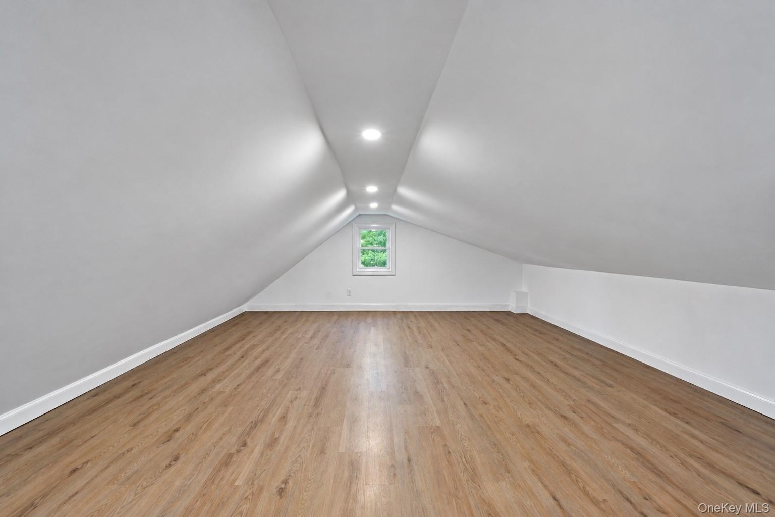 Attic space featuring vaulted ceilings, recessed lighting, wood-finish flooring, and a central window