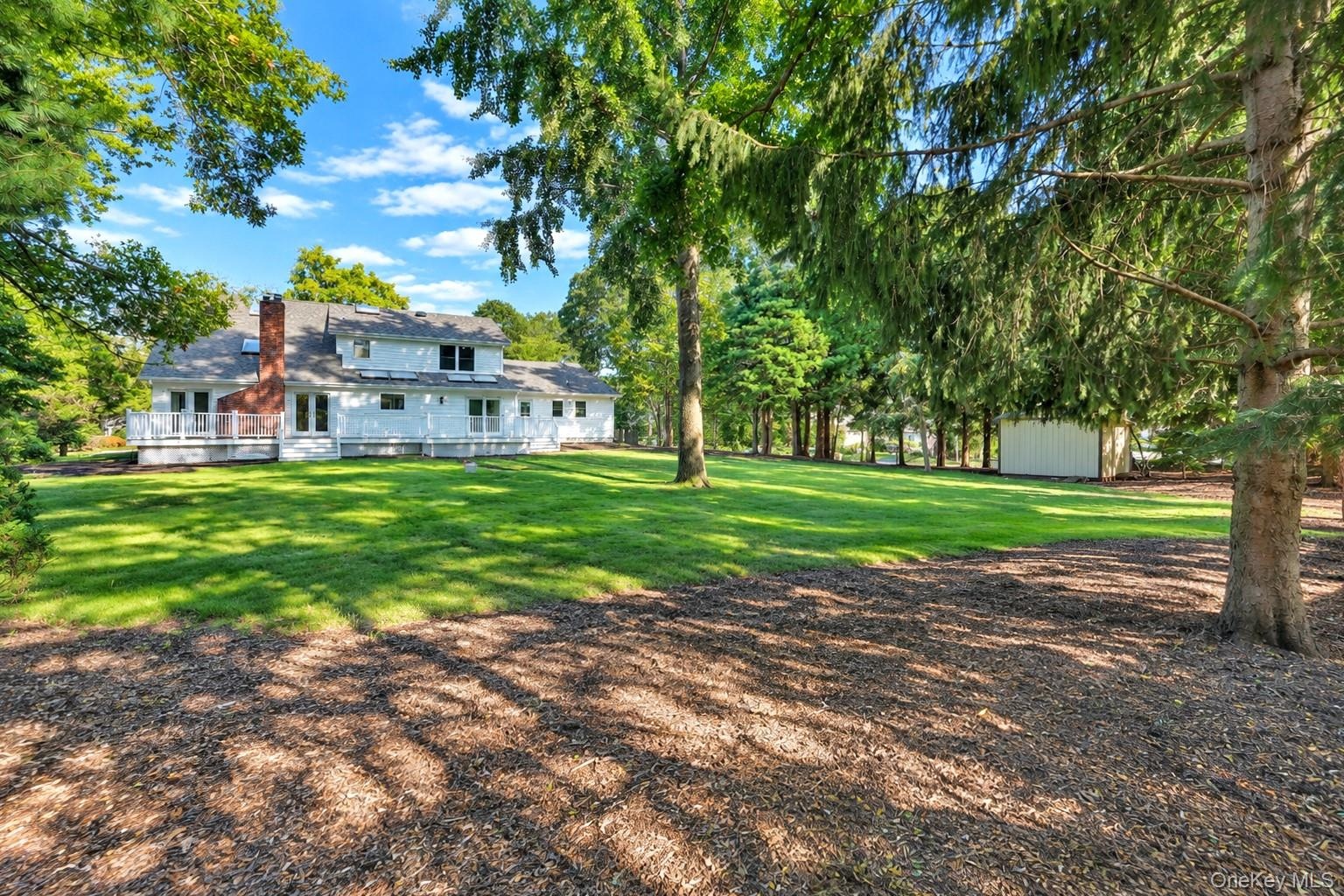 Expansive backyard featuring a manicured lawn, mature trees, a detached storage structure, and a raised wooden deck with white railing