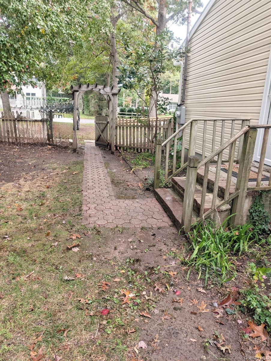 Exterior side yard featuring a paver walkway, wood garden arbor, and fencing and side door entrance...