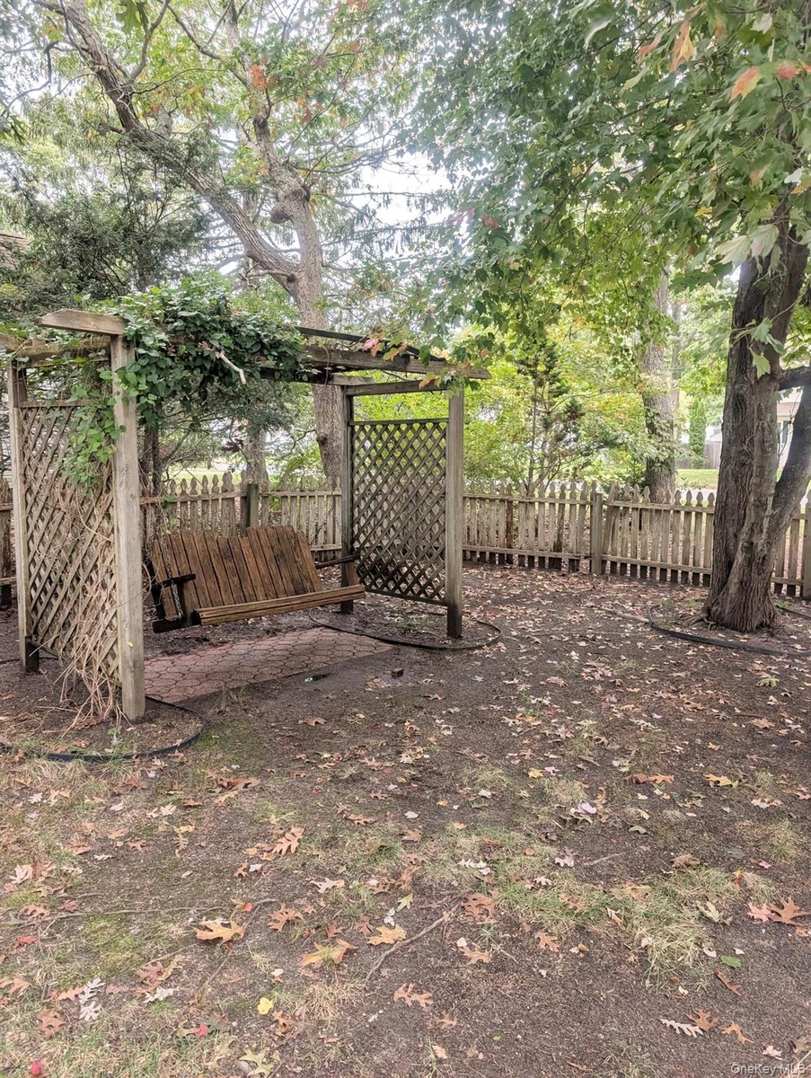 ...outdoor space featuring a wood-framed pergola with lattice sides, a suspended bench...