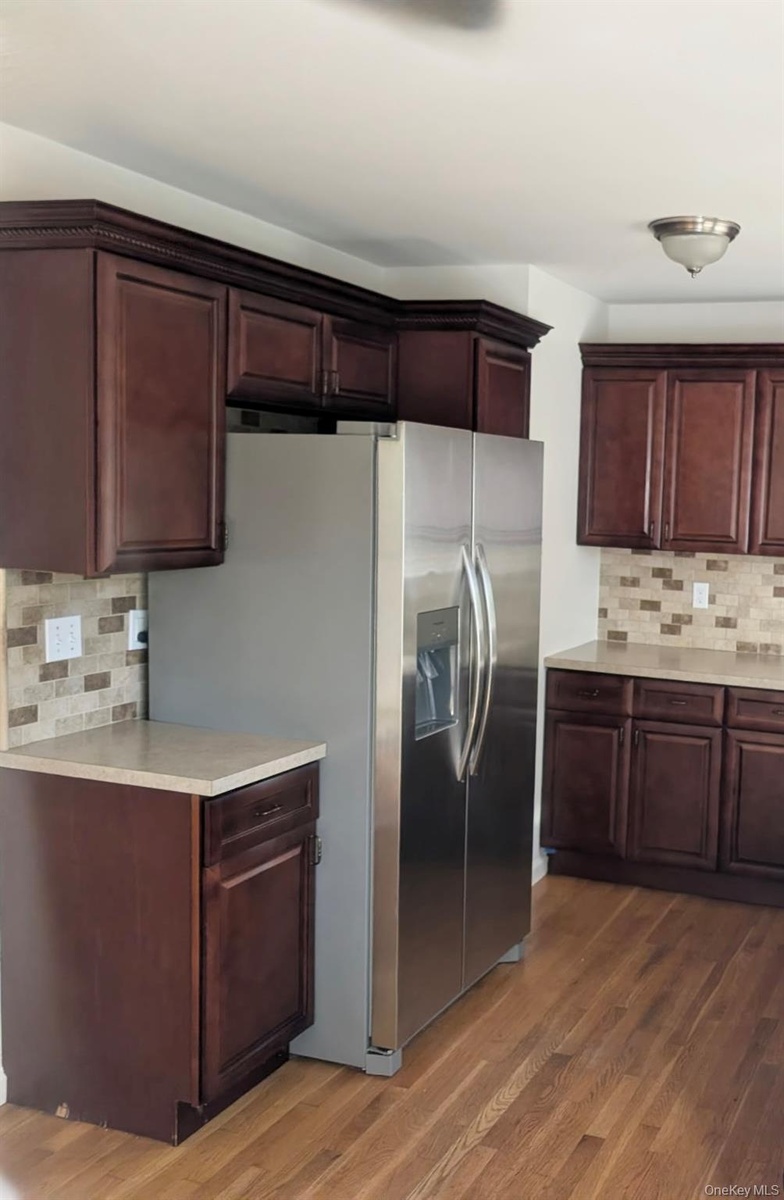 Dark wood-finish cabinetry, stainless steel refrigerator, neutral-toned solid surface countertops...