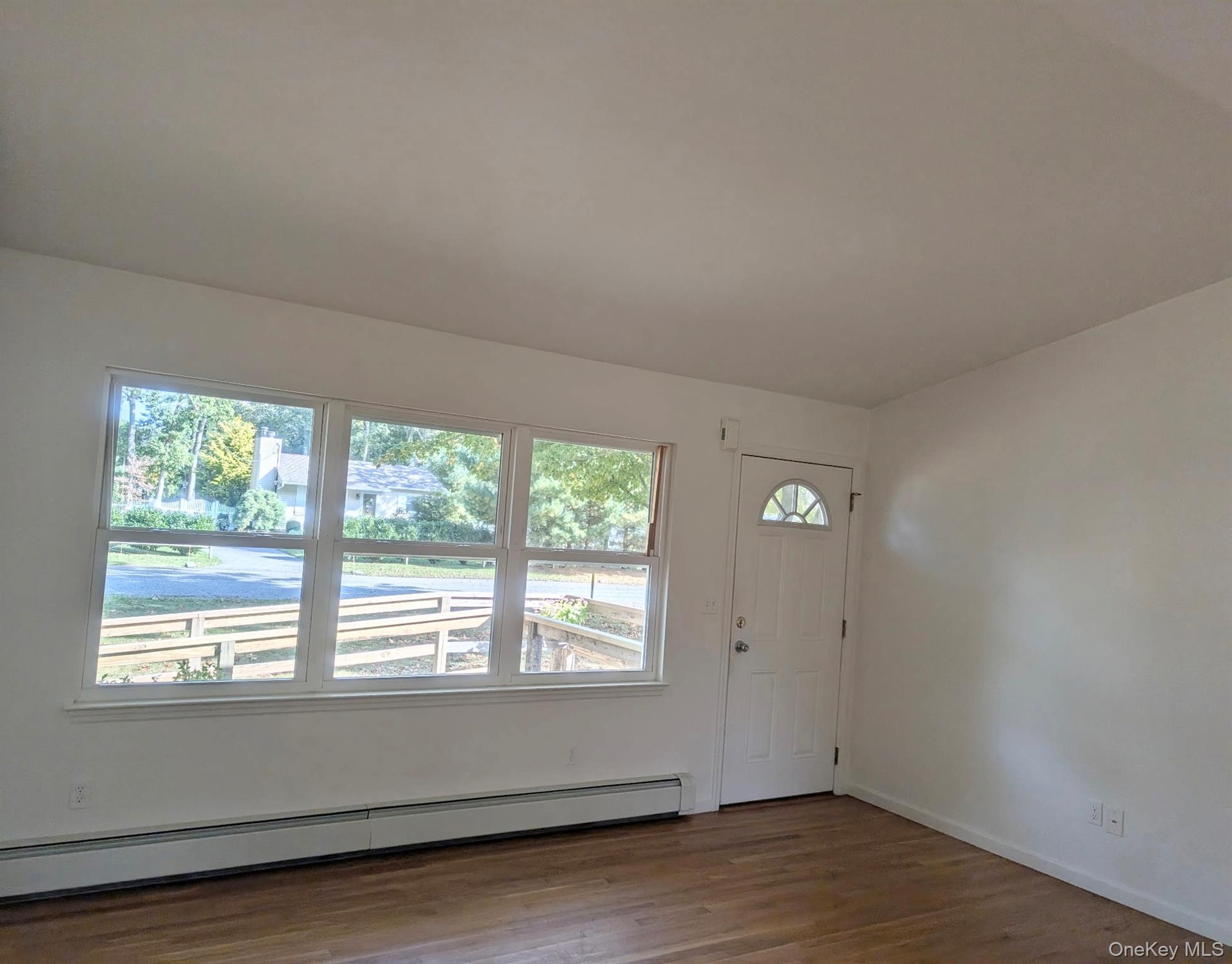 Interior space featuring expansive triple-pane windows, cathedral ceiling, wood floors, and a white entry door with a decorative glass insert.