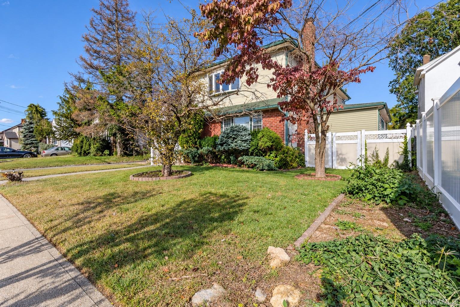 Two-story residence featuring a brick and siding exterior, a chimney, and a white privacy fence