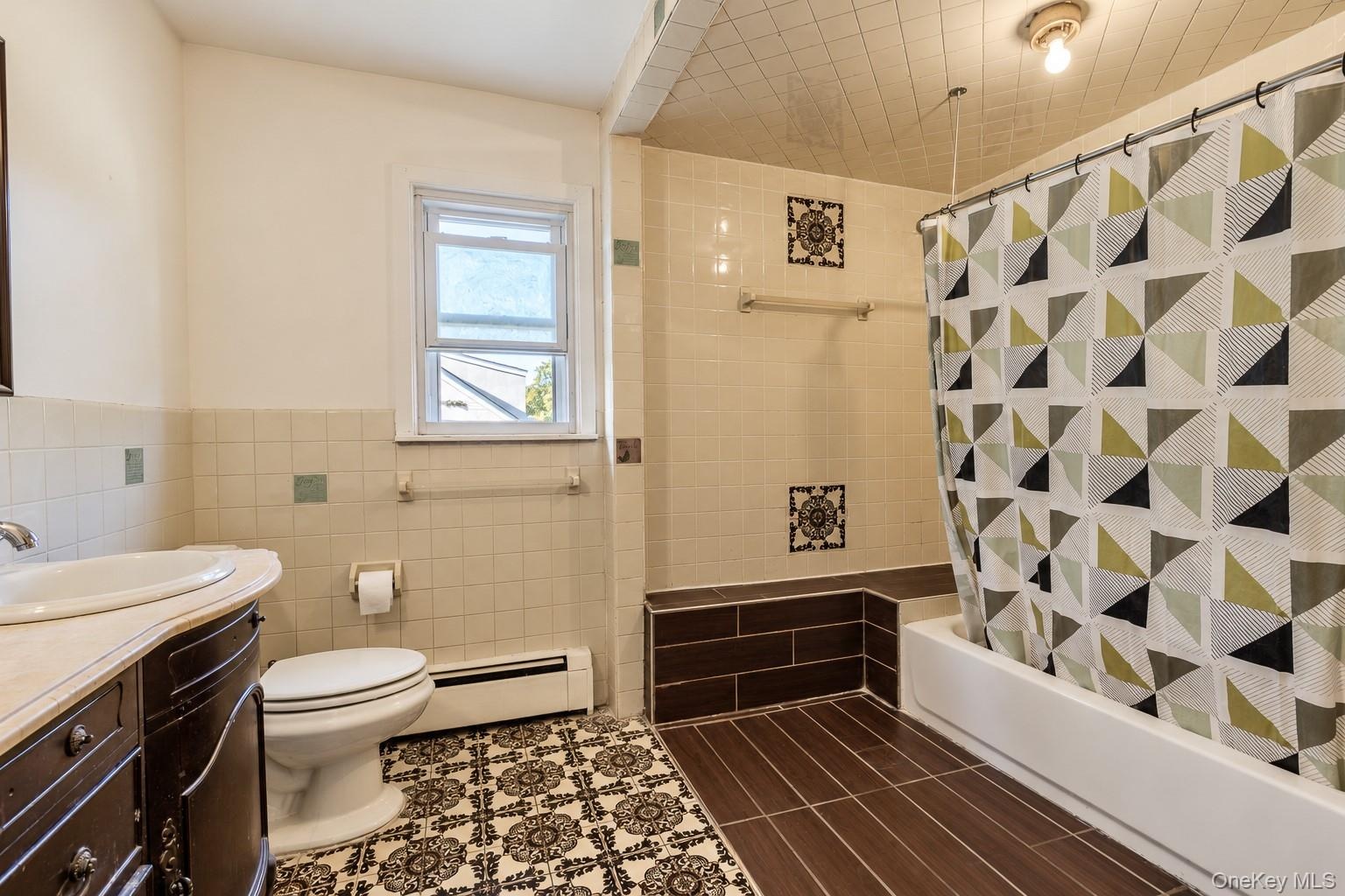 Bathroom featuring a dark wood vanity with an integrated basin, patterned tile flooring, a bathtub surround with decorative tile accents, and a textur