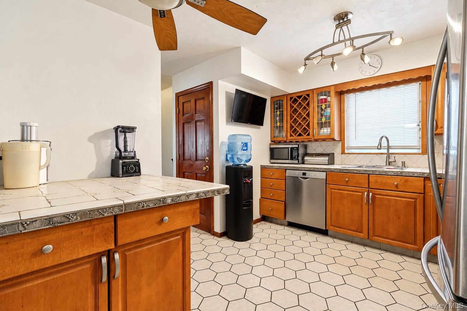Kitchen featuring tile-topped cabinetry, stainless steel dishwasher, wood-finish cabinetry with integrated wine storage, hexagonal tile flooring, and 