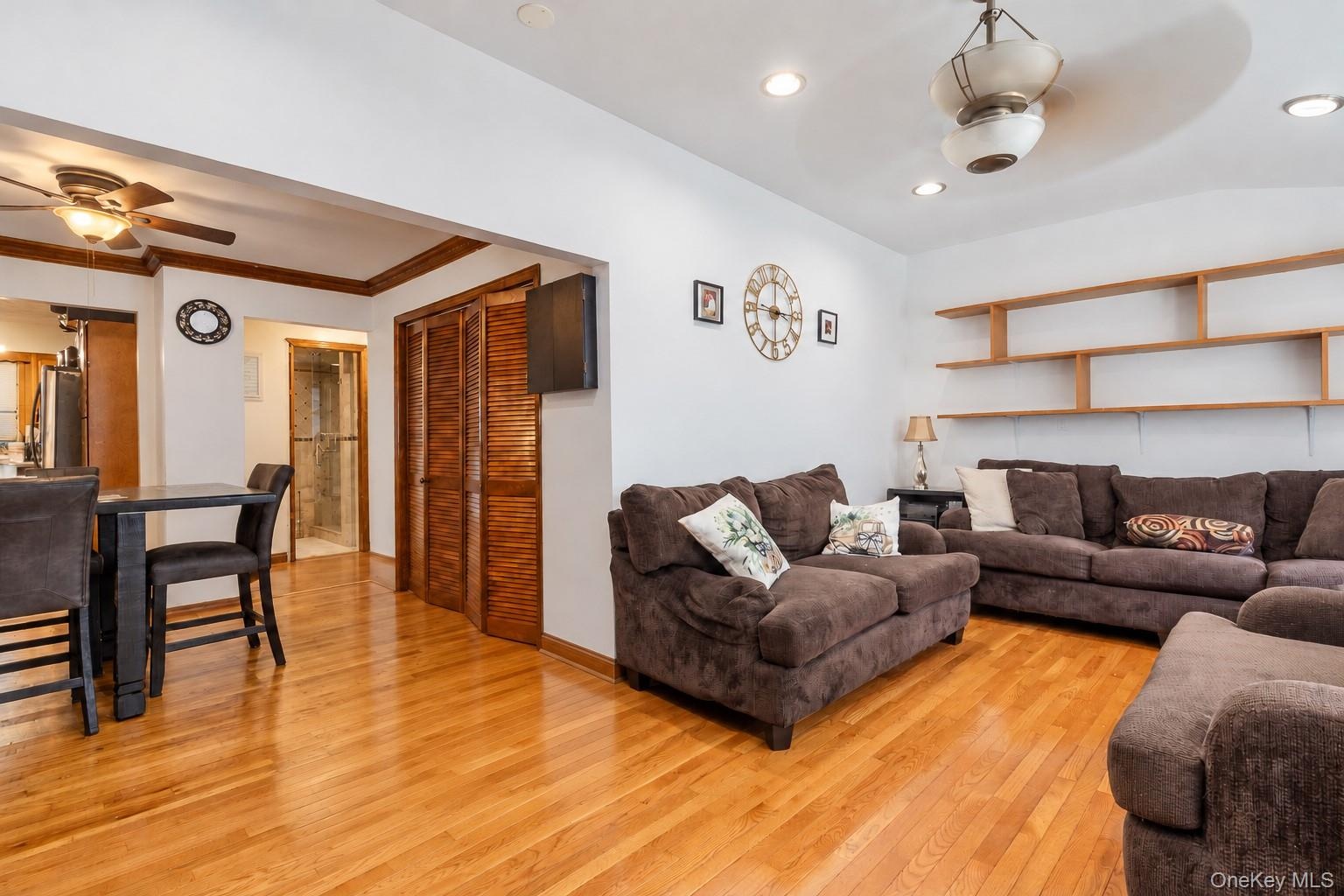 Open living area featuring wood-finish flooring, recessed lighting, ceiling fans, built-in wooden wall shelving, and wooden louvered closet doors