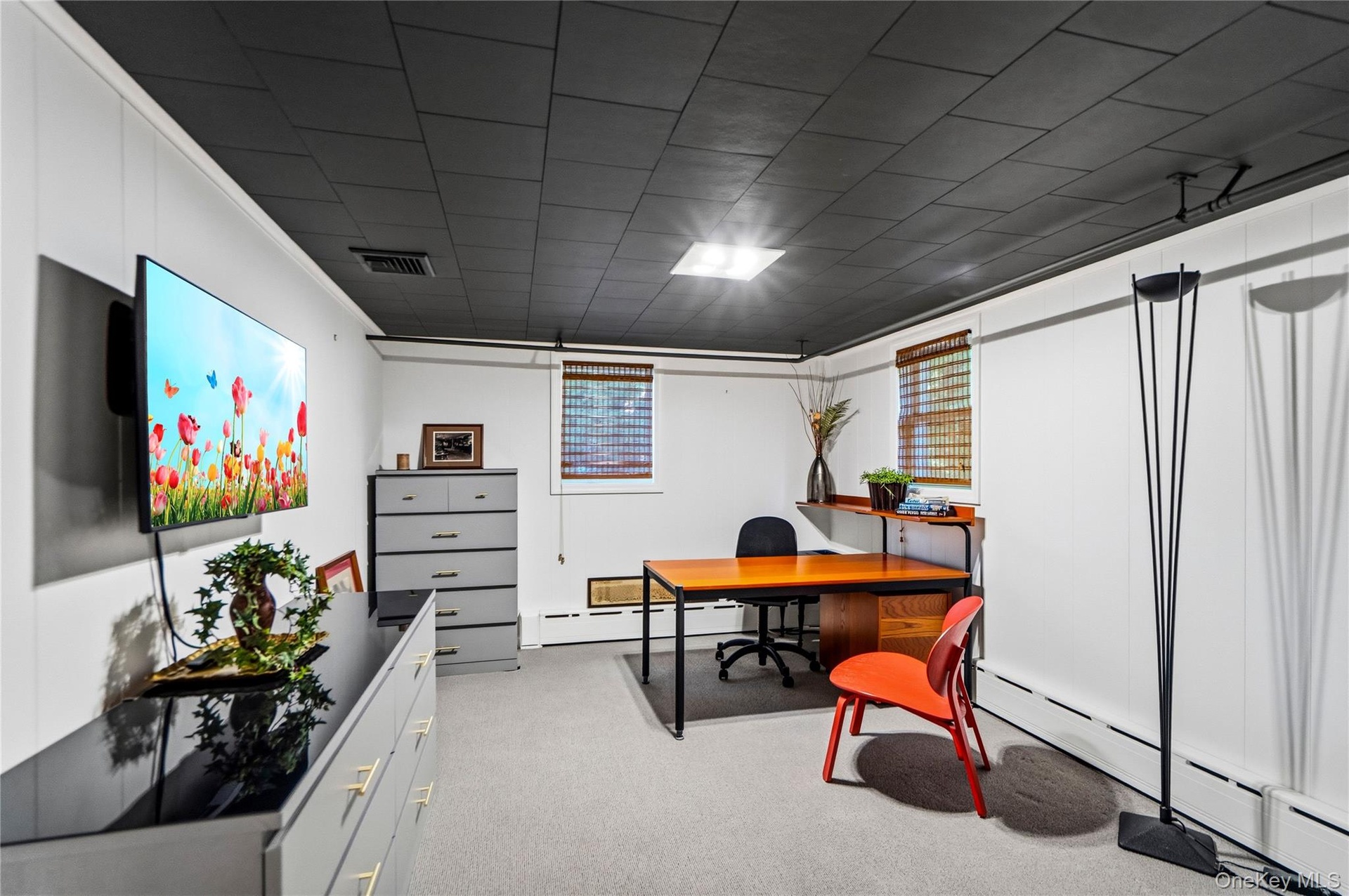 Interior space featuring charcoal-toned ceiling tiles, white wall paneling, neutral carpeting, and built-in shelving