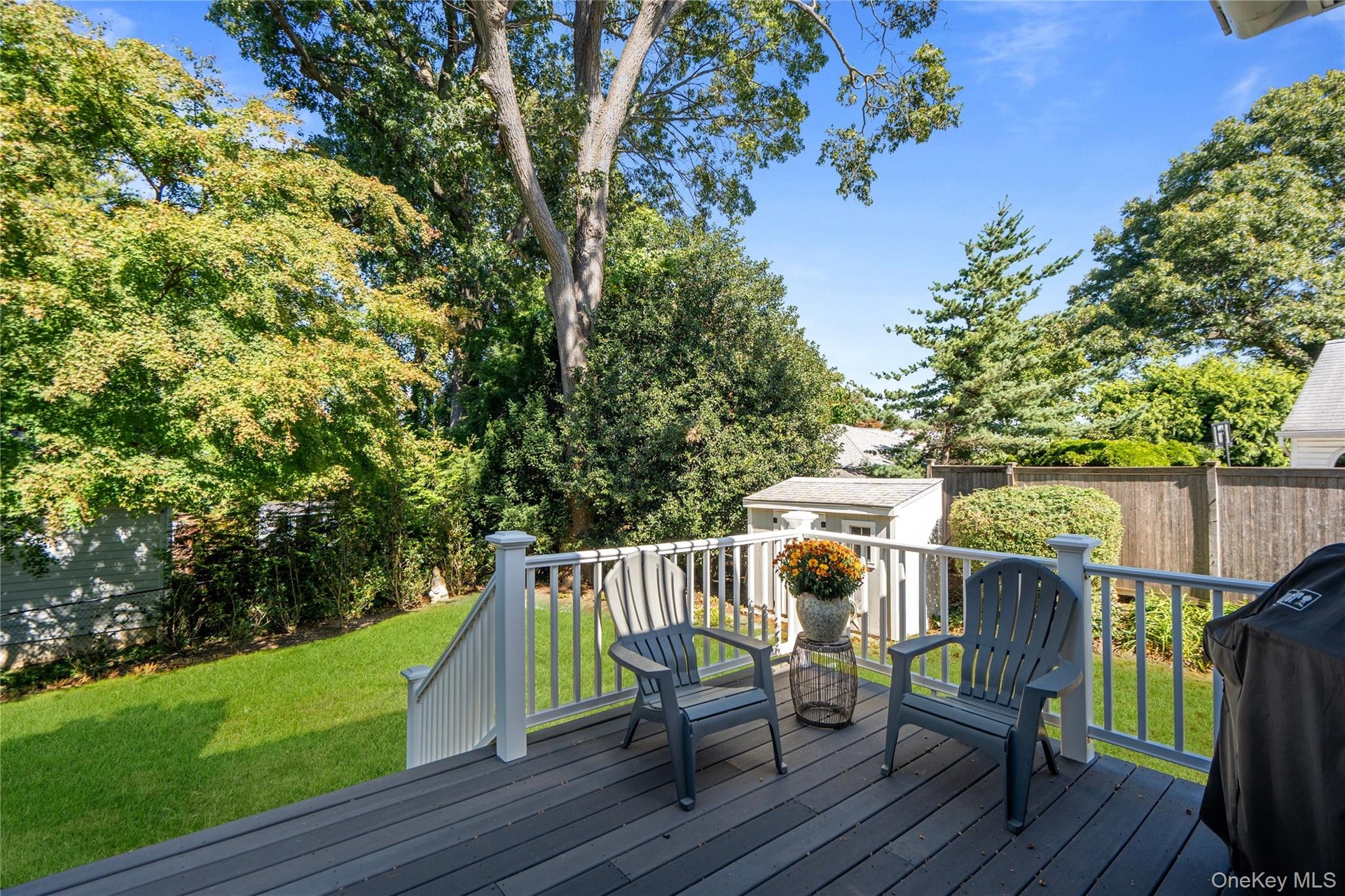 Elevated deck Trex deck featuring Azak railings, a manicured lawn,  fenced backyard, and mature trees