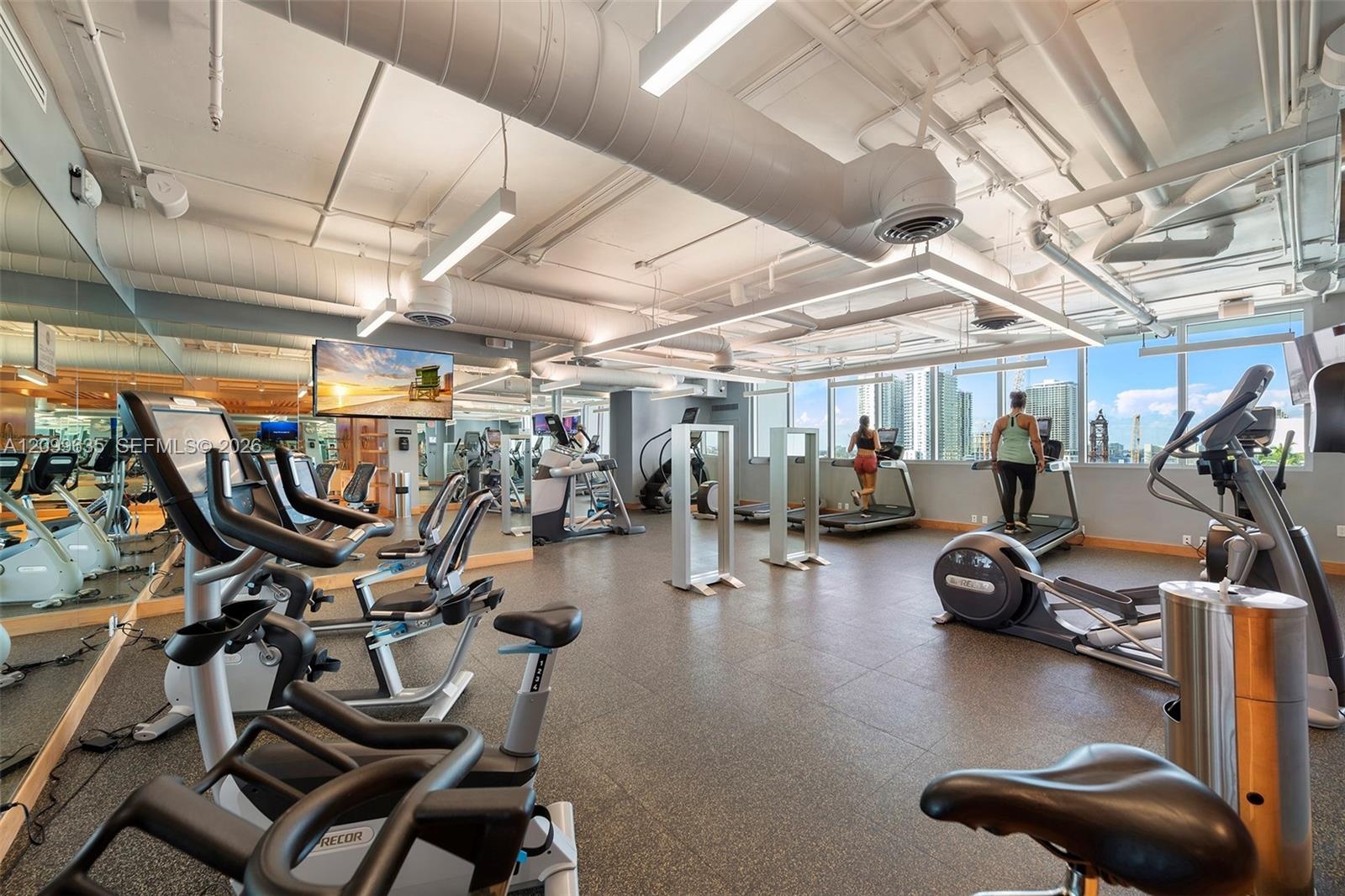Fitness center featuring expansive floor-to-ceiling windows, exposed ductwork, recessed and linear lighting, and rubberized flooring