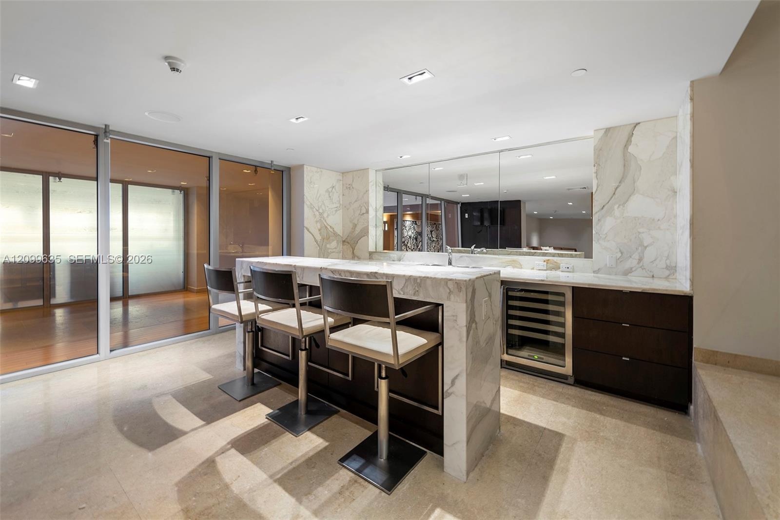 Marble-clad wet bar with integrated wine refrigeration, deep-toned cabinetry, and reflective wall paneling