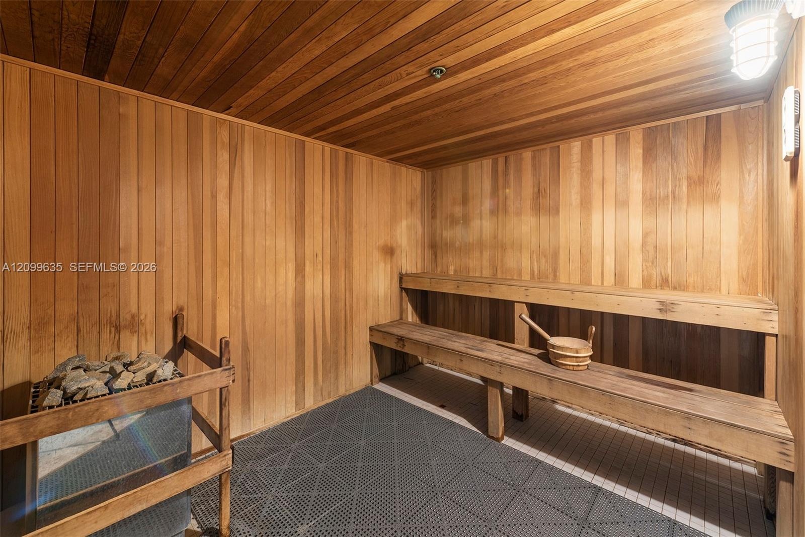 Wood-paneled sauna featuring a slatted wood ceiling, a built-in wood bench, and a sauna heater with stones
