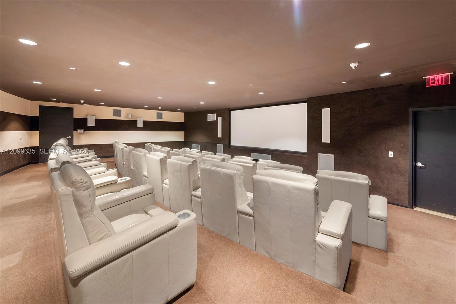 Dedicated media room with stadium-style seating, recessed ceiling lighting, a large projection screen, and wall-mounted speakers