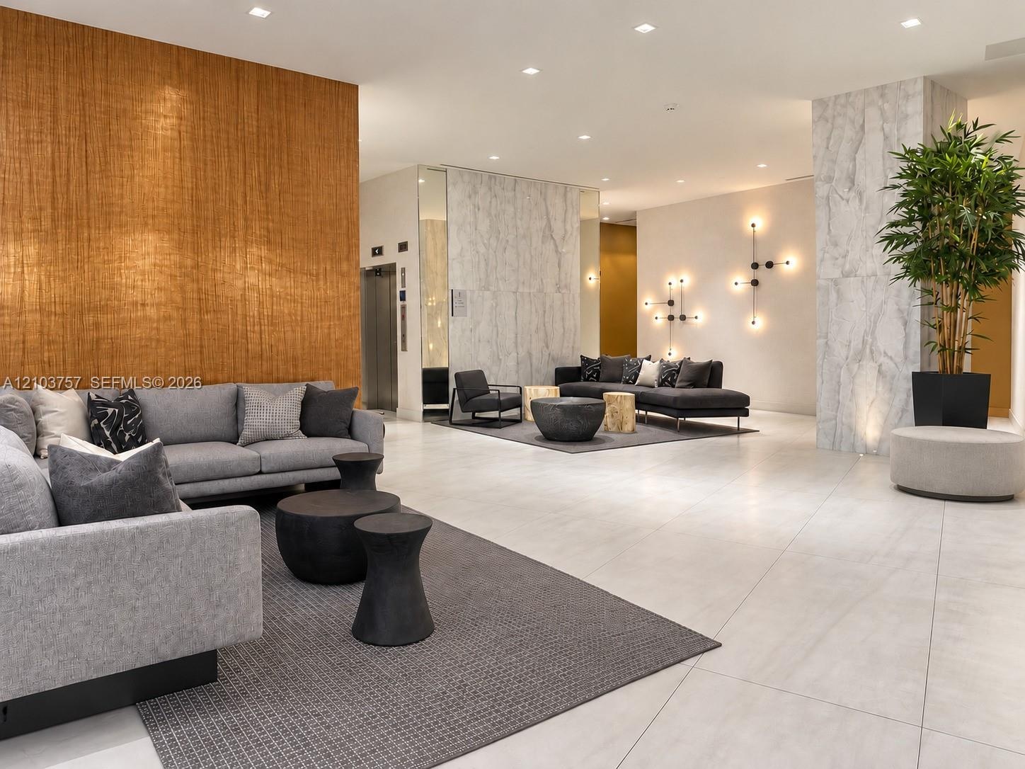 Spacious common area featuring textured accent wall, light stone tile flooring, and modern wall sconces