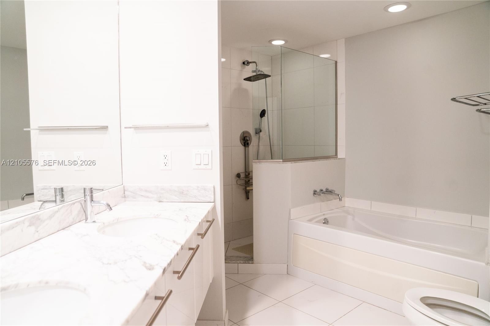 Dual-sink vanity with stone-finish countertop, walk-in shower with glass enclosure and rainfall showerhead, and a deep soaking tub with wall-mounted c