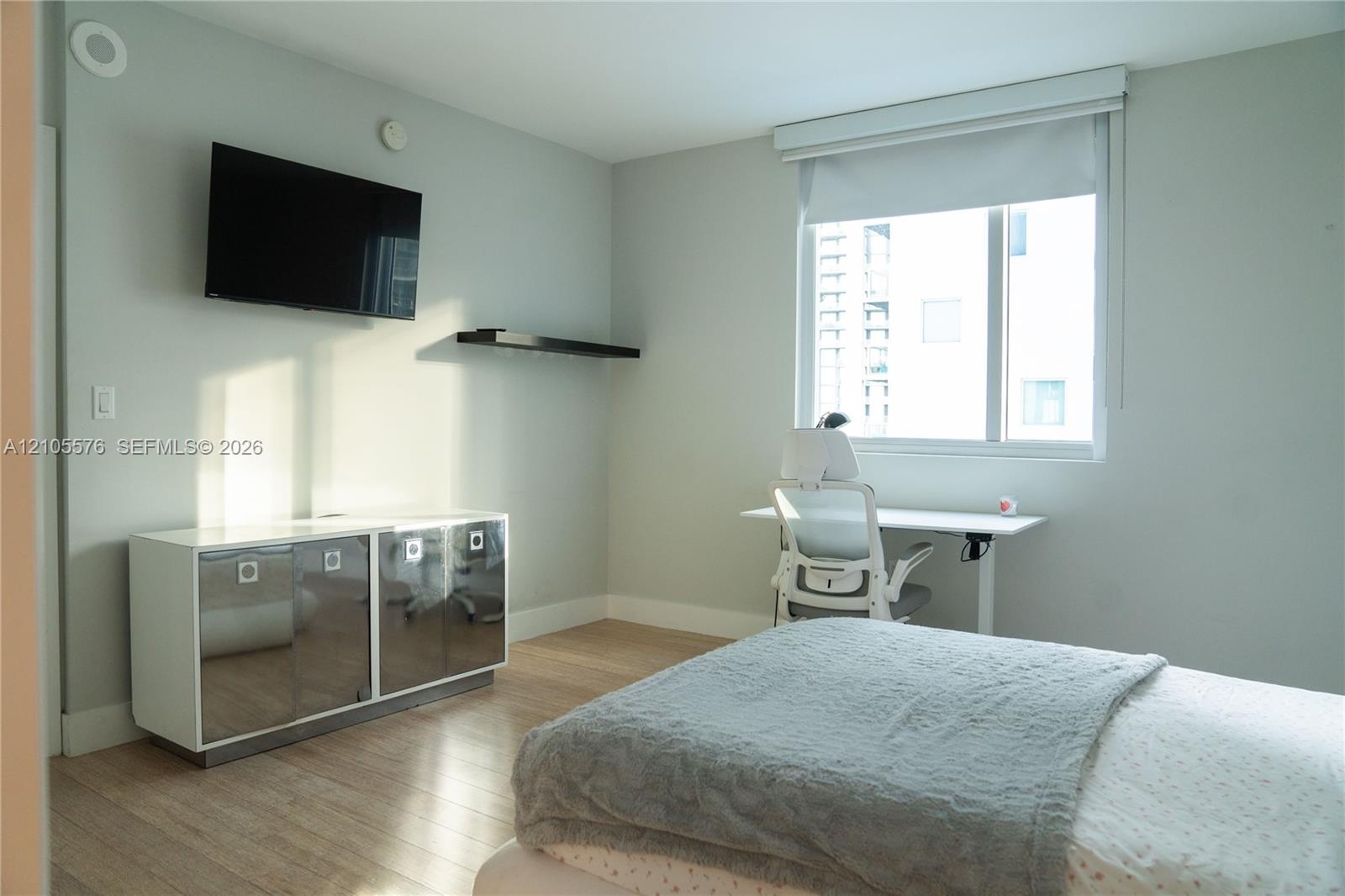 Room featuring wood-finish flooring, a wall-mounted floating storage unit with reflective finish, a fixed wall-mounted shelf, and a large window with 