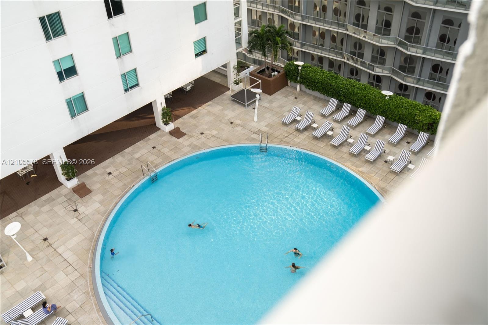 Circular swimming pool with integrated stair entry, surrounded by a stone-tiled deck and manicured hedge landscaping