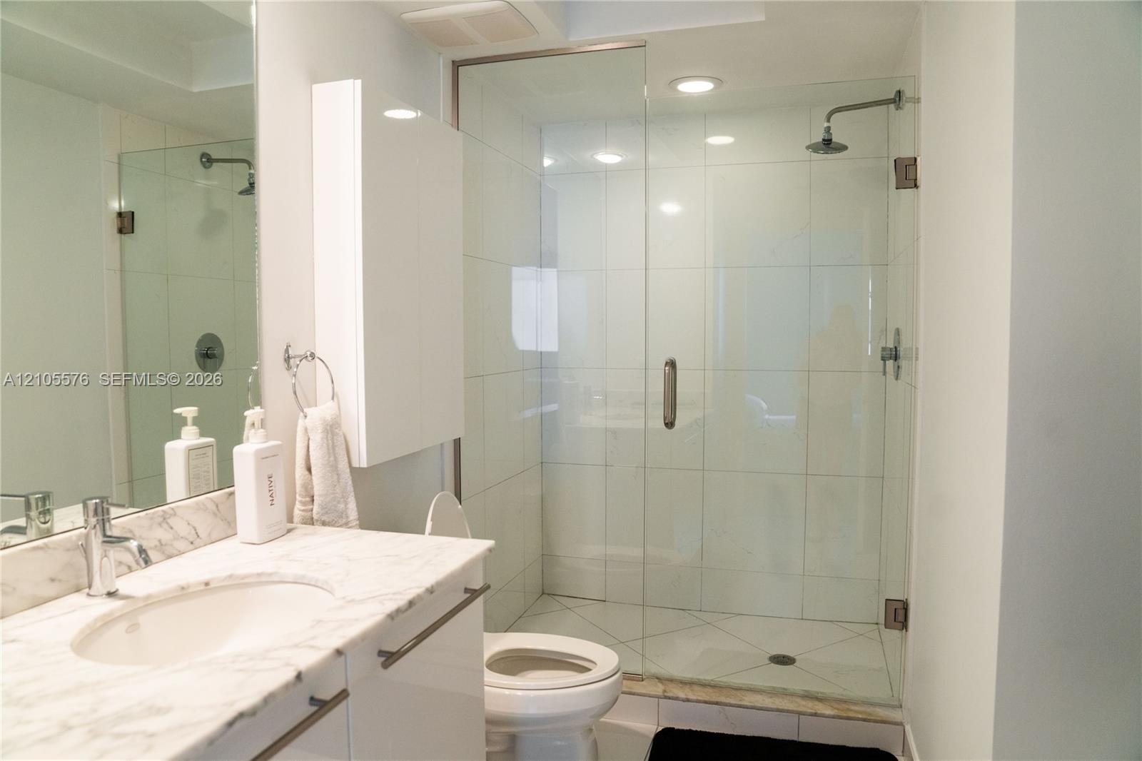 Bathroom featuring a stone-top vanity with an undermount sink, glass-enclosed shower with tile surround, and recessed lighting