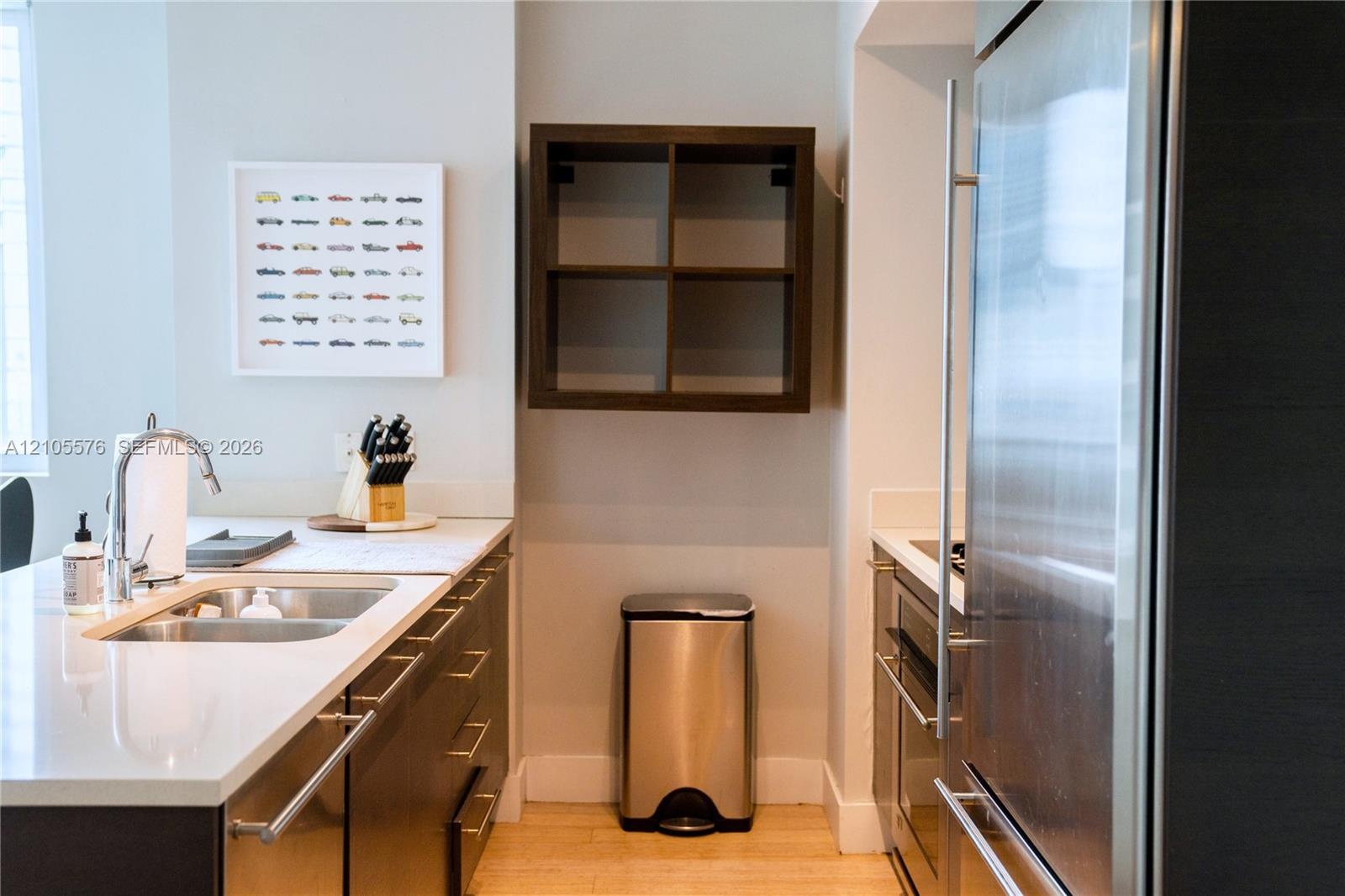 Kitchen featuring flat-panel dark cabinetry, white countertops, integrated stainless steel refrigerator, undermount double-basin sink with a gooseneck