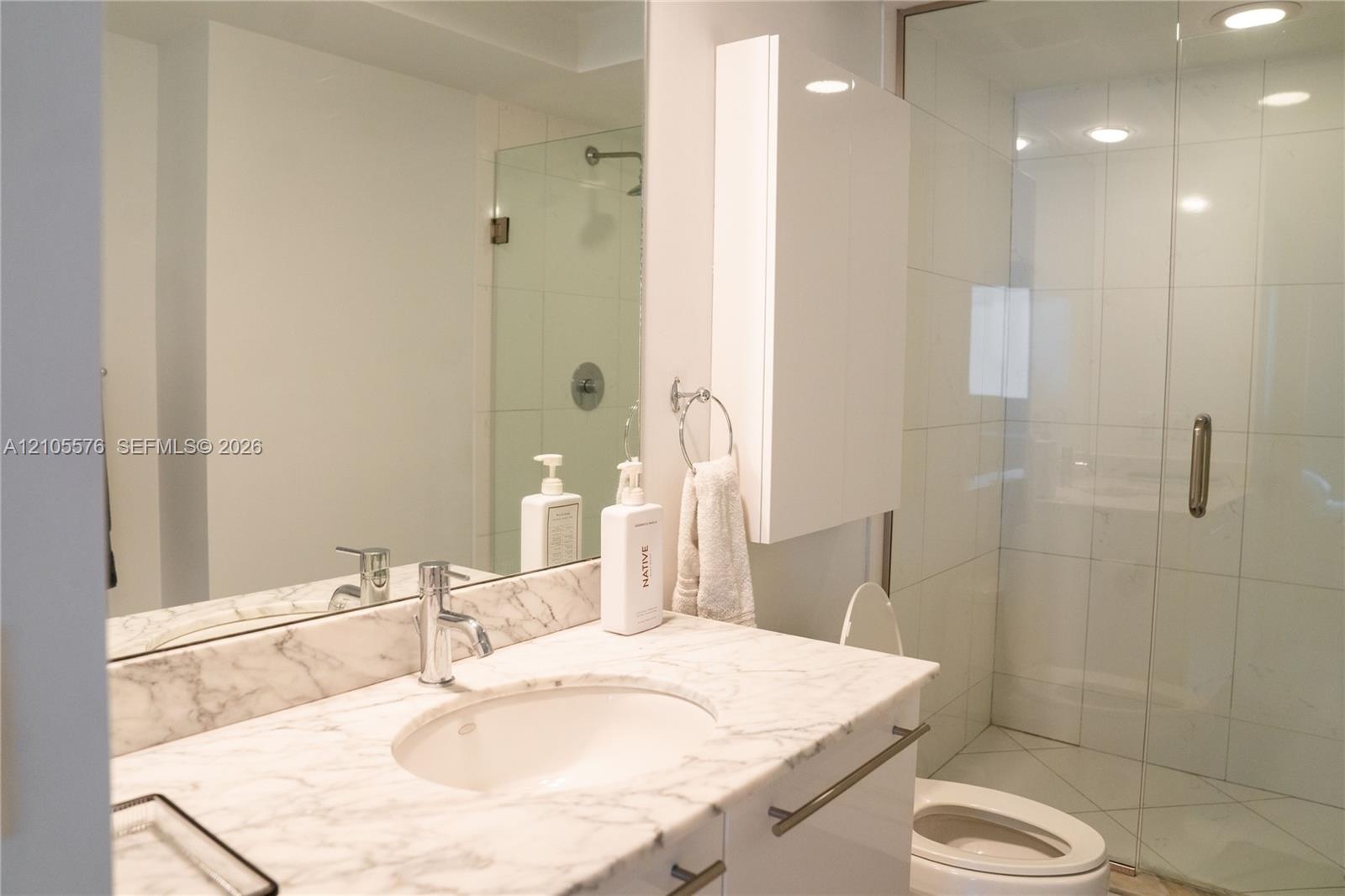 Bathroom featuring a stone-surface vanity with an integrated basin, wall-mounted medicine cabinet, full-width mirror, and a glass-enclosed walk-in sho