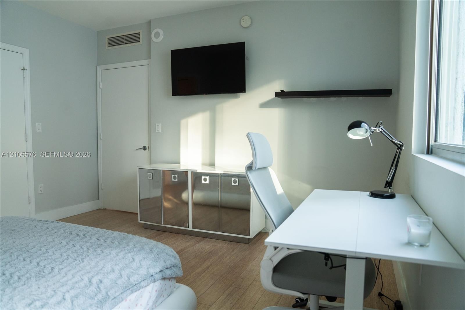 Wood-finish flooring, built-in lower cabinetry with metallic finish doors, and a wall-mounted floating shelf