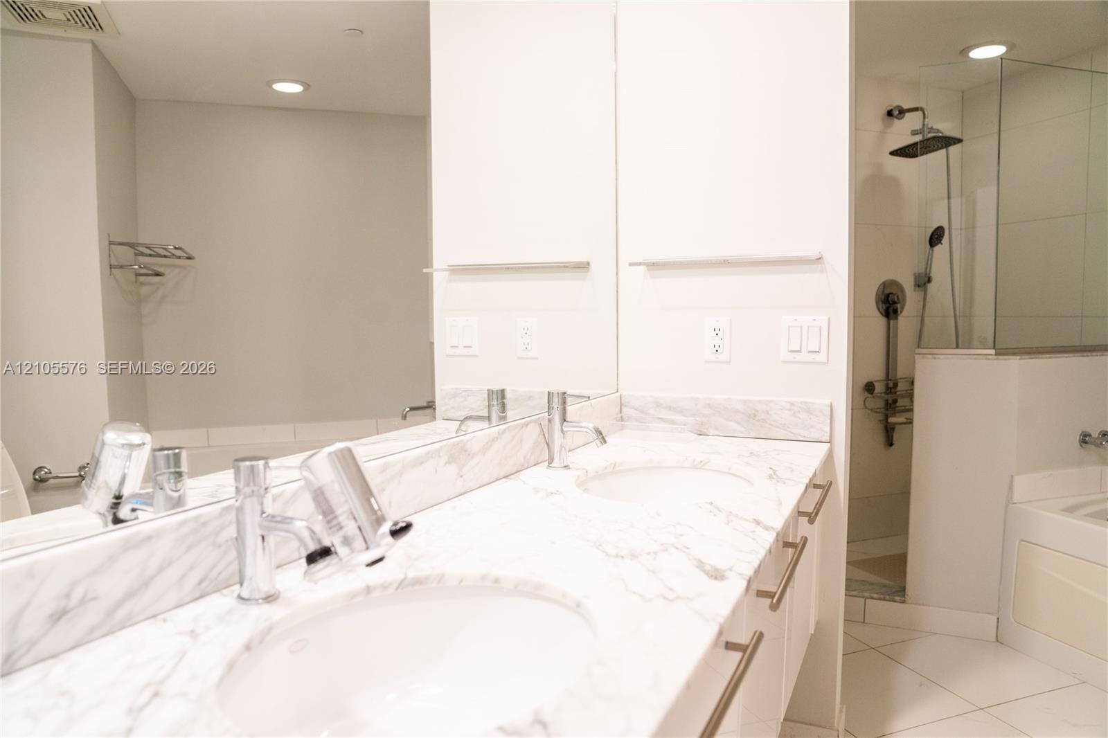 Dual-sink vanity with stone-finish countertops, polished chrome faucets, a full-width wall mirror, and a glass-enclosed shower with a rainfall showerh