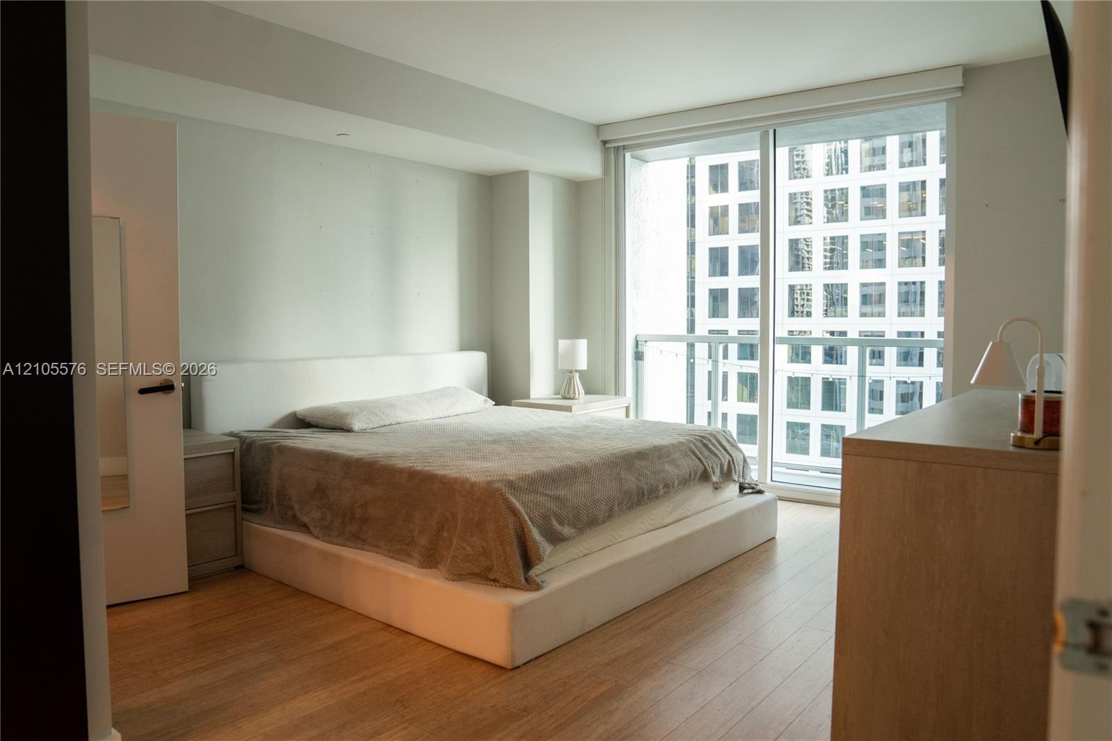 Floor-to-ceiling windows with integrated glass balcony railing, wood-finish flooring, and neutral wall tones