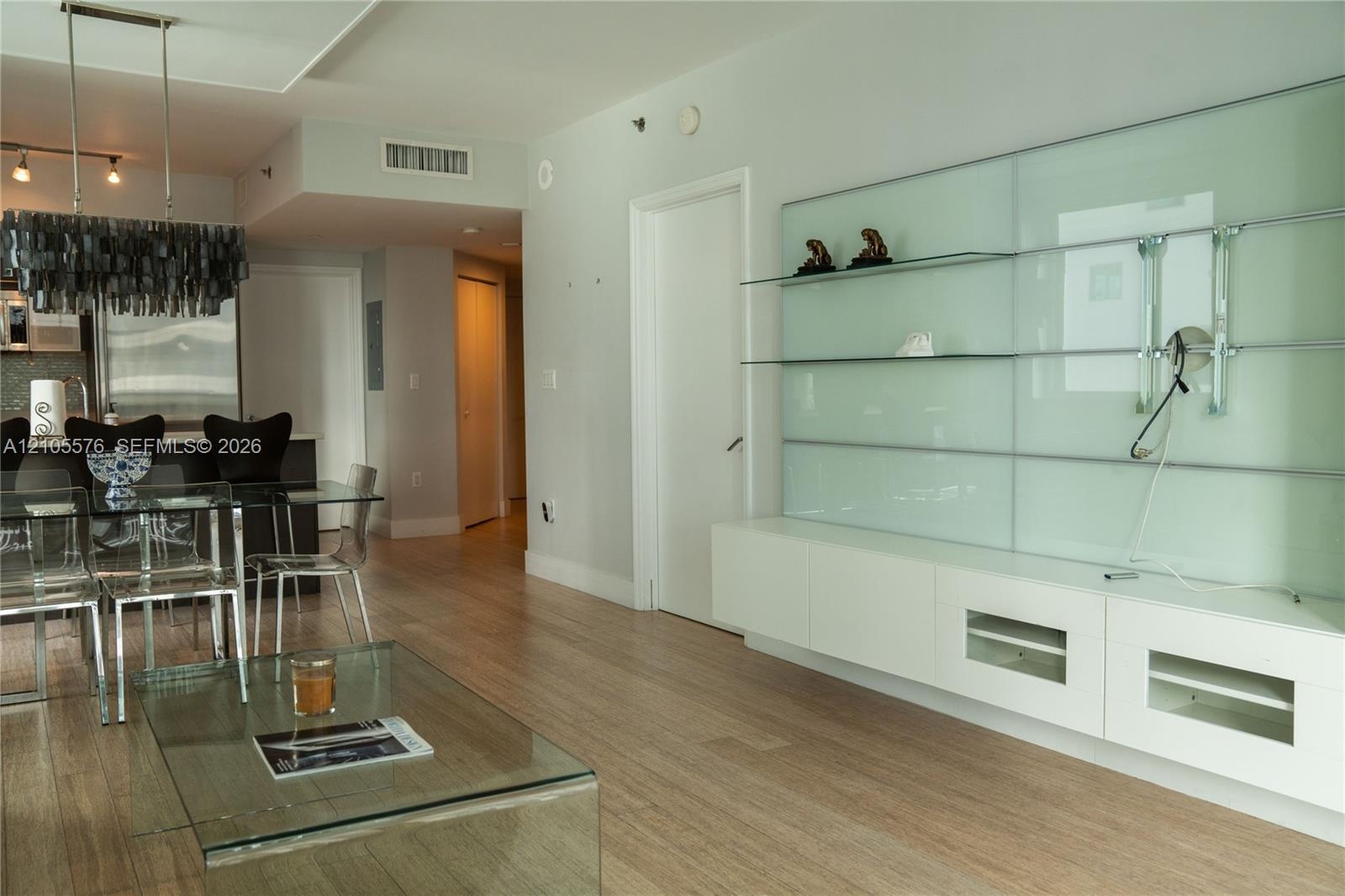 Wood-finish flooring, custom built-in white cabinetry with glass shelving, and a linear pendant light fixture