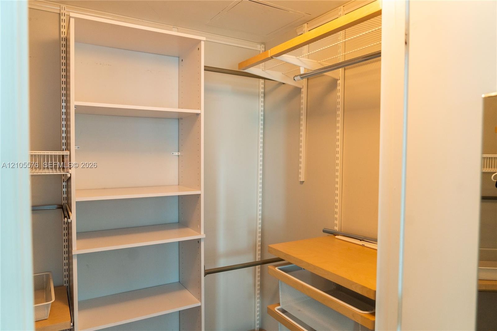 Walk-in closet featuring white adjustable shelving, integrated metal clothing rods, wood-finish shelving, and built-in sliding drawer units