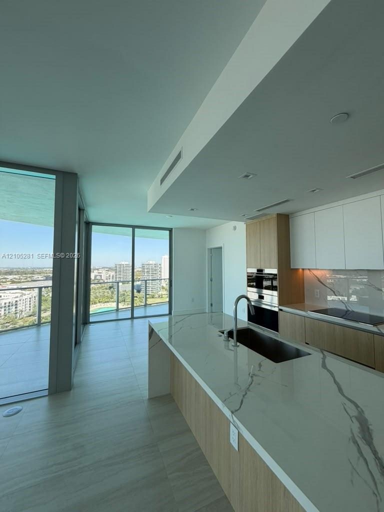 Kitchen featuring a waterfall-edge island with stone-finish countertops, flat-panel cabinetry, built-in stainless steel appliances, and floor-to-ceili