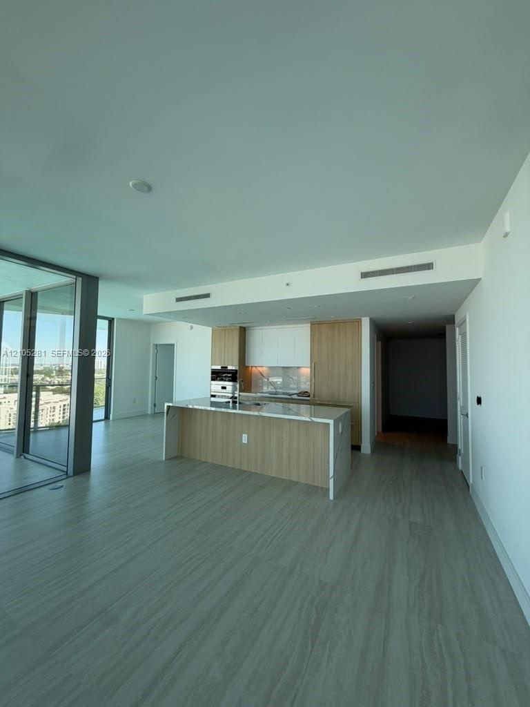 Kitchen featuring custom wood-finish cabinetry, a waterfall-edge stone countertop, built-in stainless steel oven, and expansive floor-to-ceiling glass