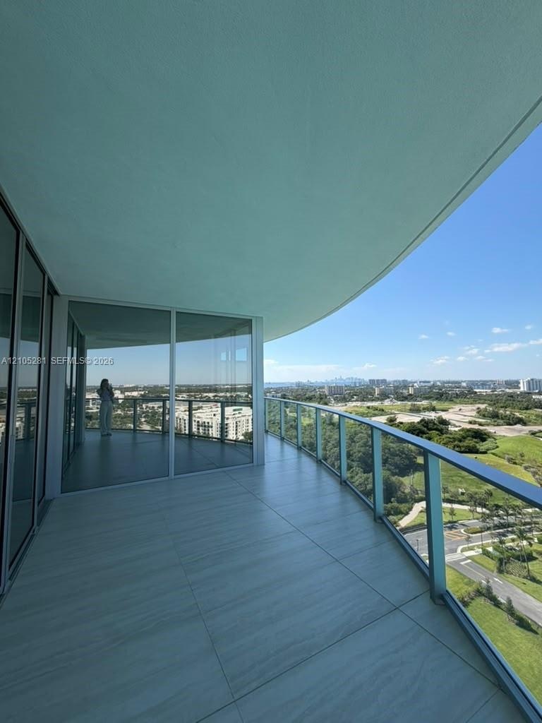 Expansive covered terrace featuring large-format tile flooring, curved architecture, and a glass-paneled railing